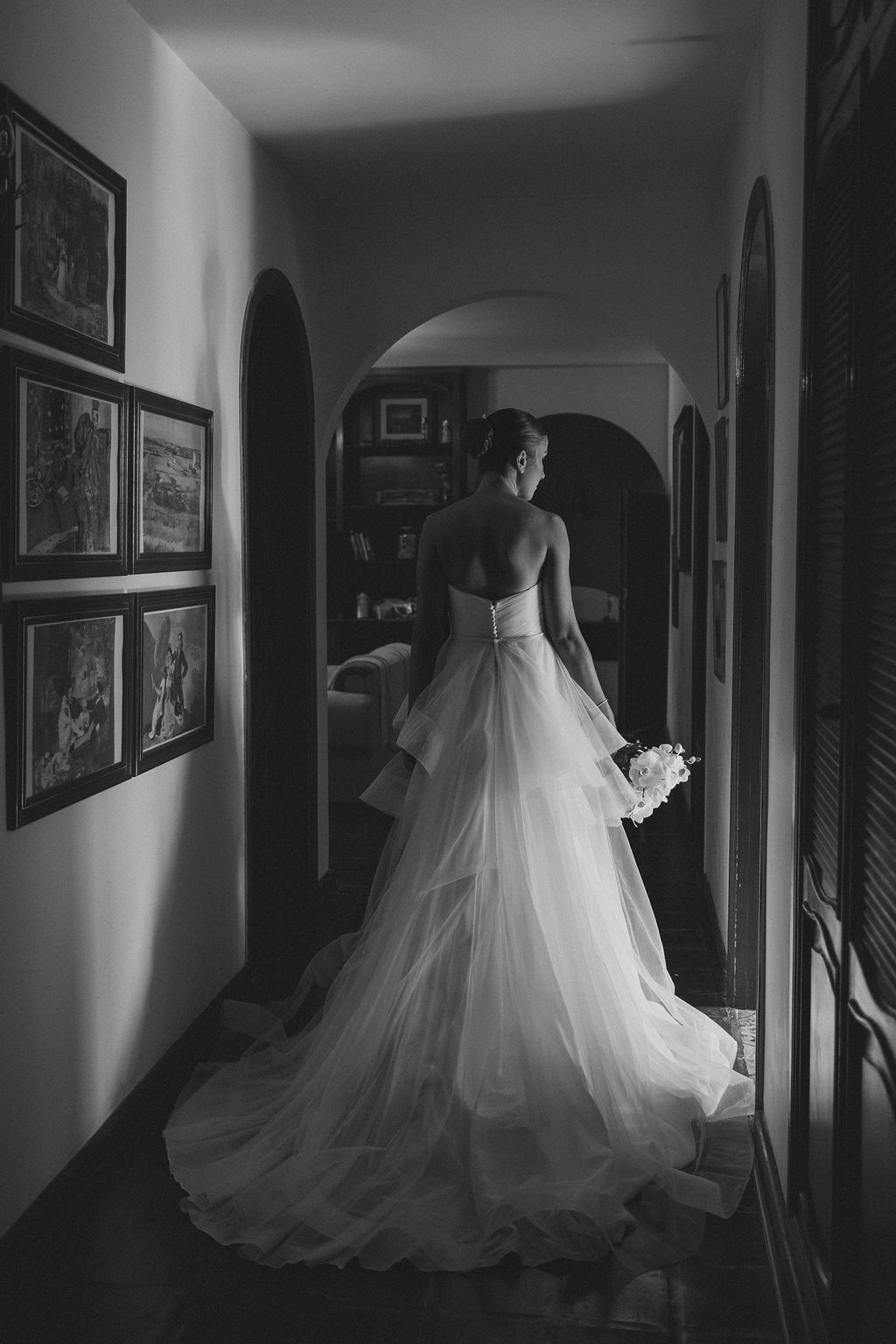 Dramatic black and white bridal portrait showing a flowing white wedding gown with long train in an arched hallway.