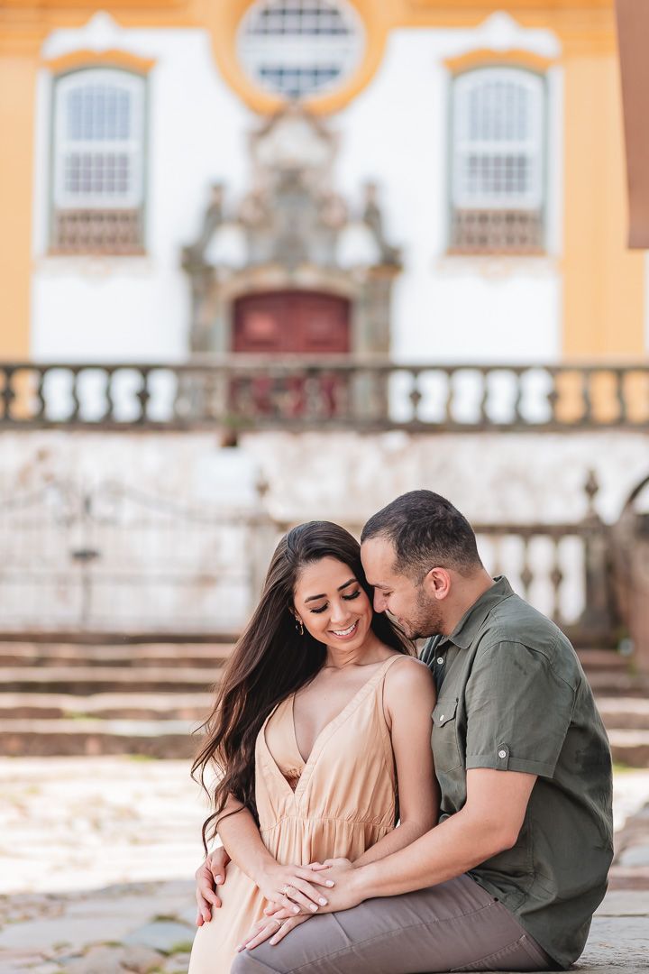Romantic couple shares an intimate moment sitting on stone steps outside a historic colonial church in warm afternoon light.