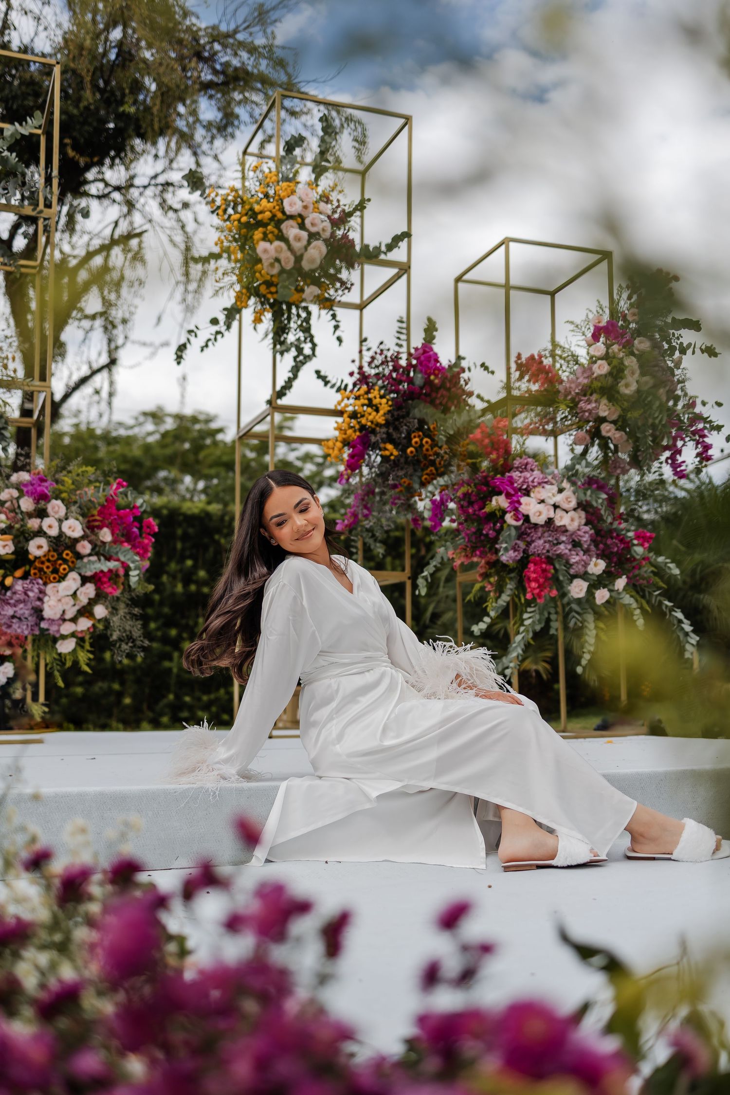 Elegant white dress against vibrant floral backdrop with geometric gold frames and purple blooms in outdoor garden setting.
