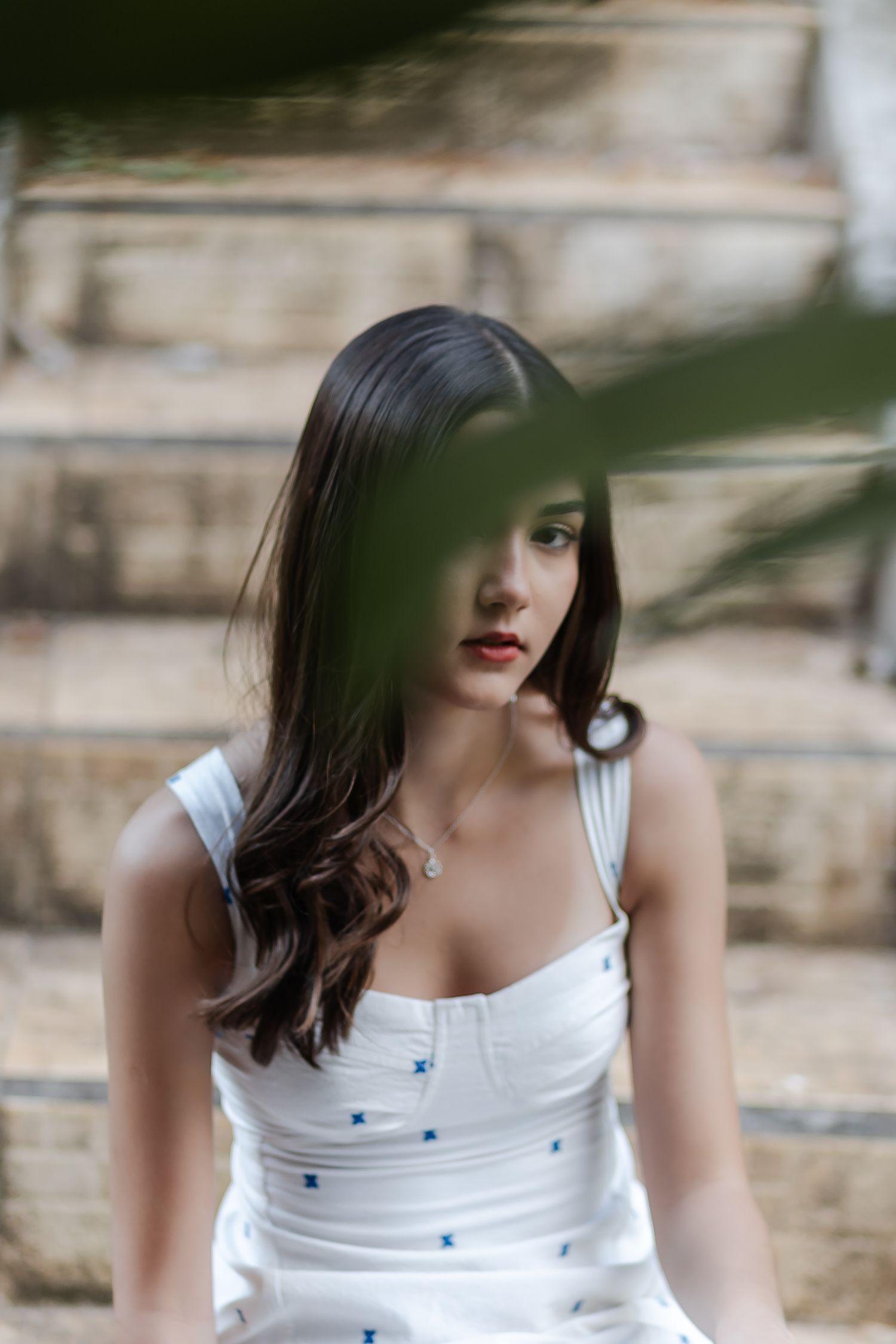 Motion sequence shows a person with dark hair wearing a white dress with blue details against a stone wall background.
