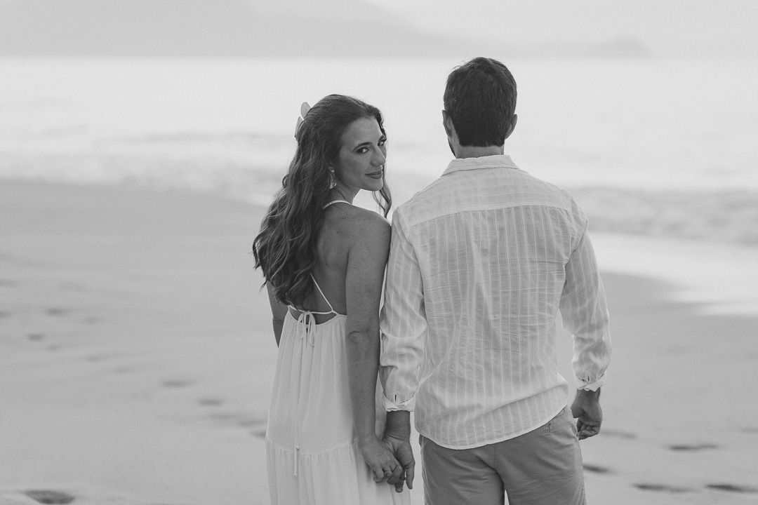 A couple walking together on a beach in black and white, the woman looking back over her shoulder.