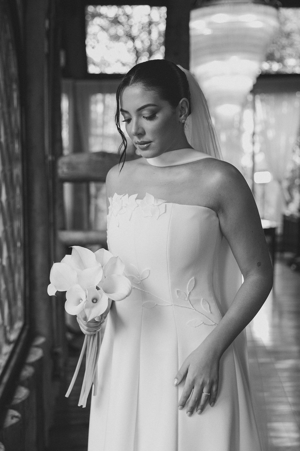 Fotógrafo de casamento em SP, AlfA bride in an elegant strapless white wedding gown holds a white orchid bouquet in a naturally lit hallway.
