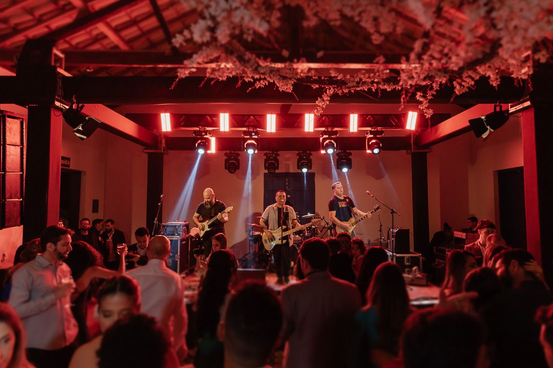 A live band performs on stage in a red-lit concert venue with an energetic crowd watching in the foreground.