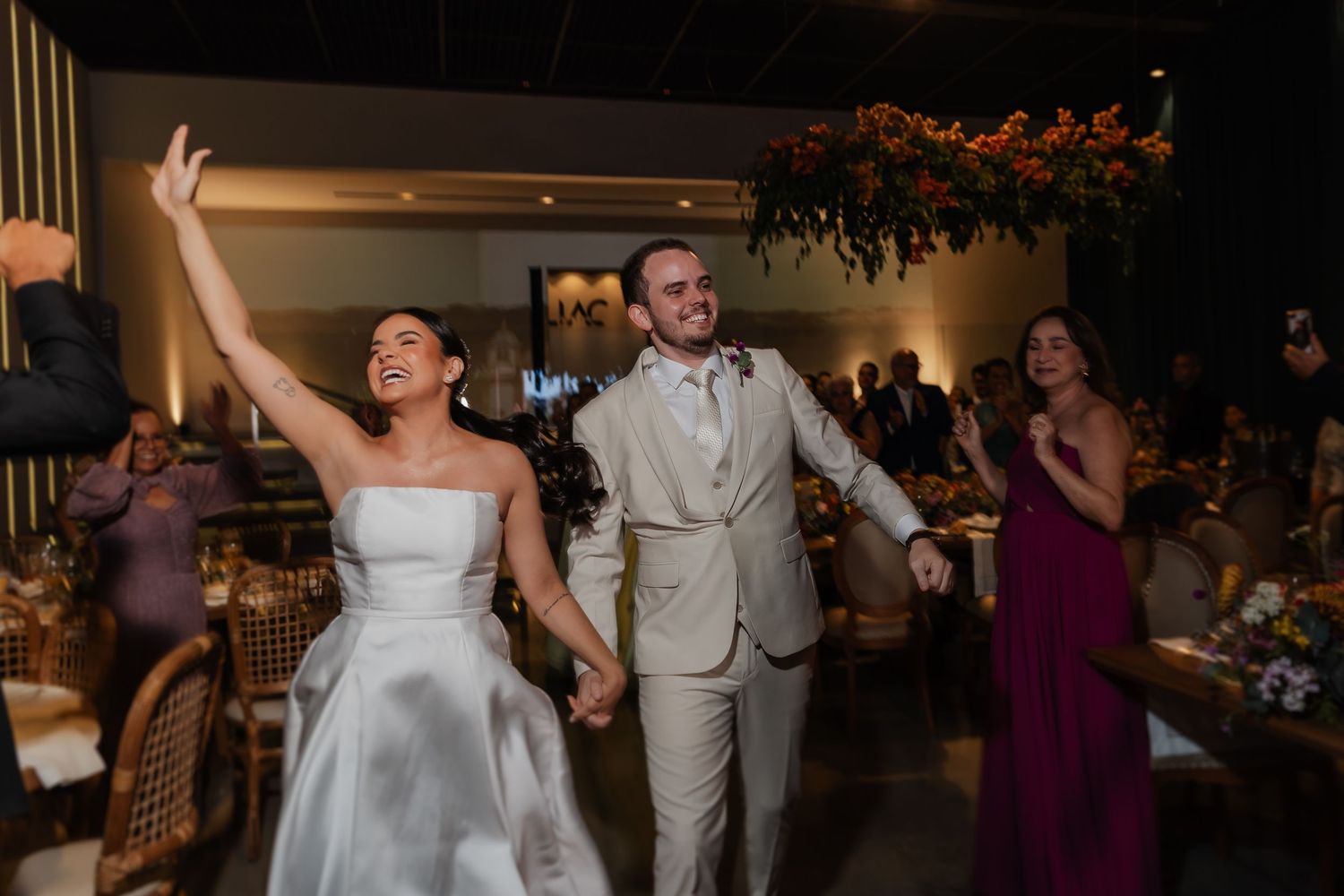 A newly married couple makes their grand entrance at a wedding reception, celebrating with joyful arms raised.