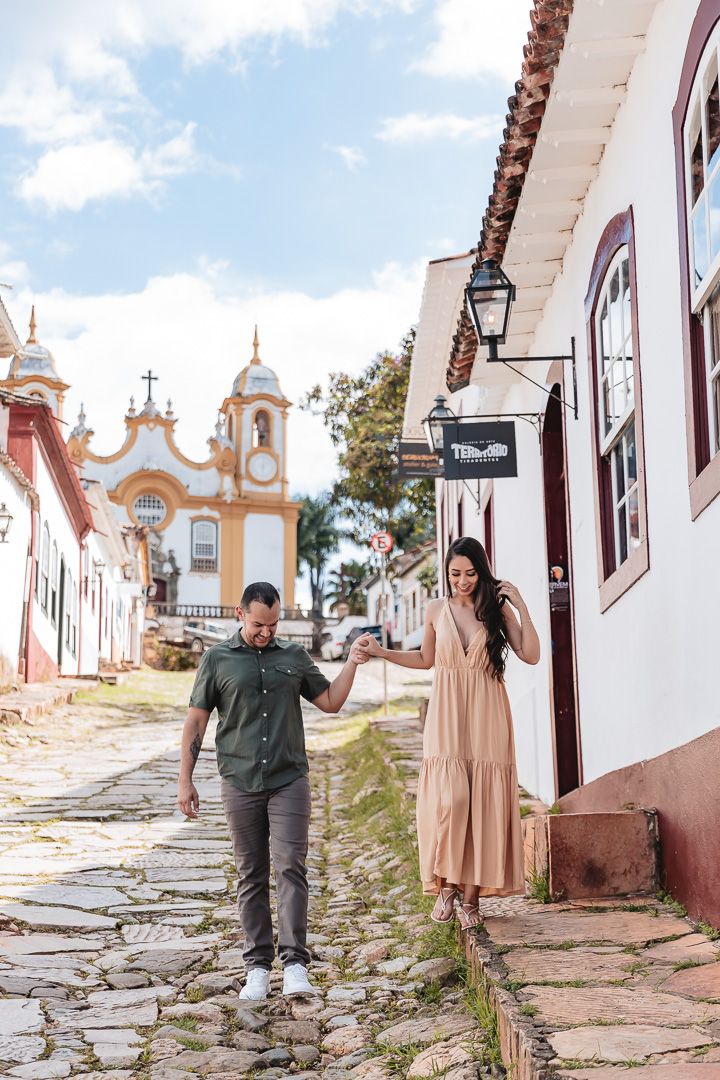 Couple exploring cobblestone streets of Tiradentes, Brazil with historic baroque church and colonial architecture in background.