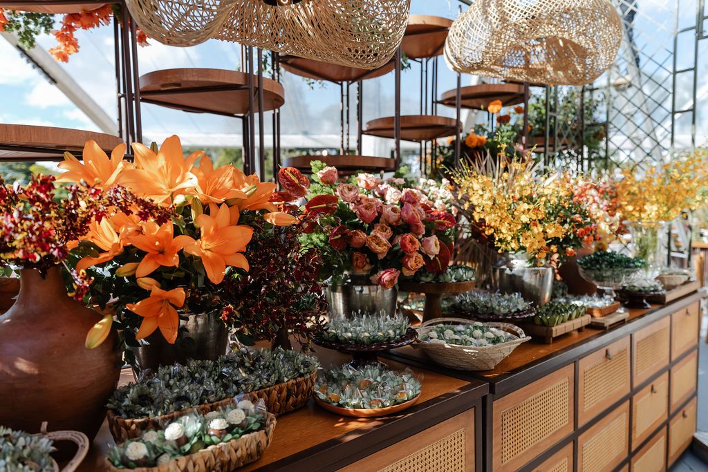 Cerimônia de casamento ao arVibrant orange lilies and floral arrangements displayed on rustic wooden tables under woven parasol decorations.
