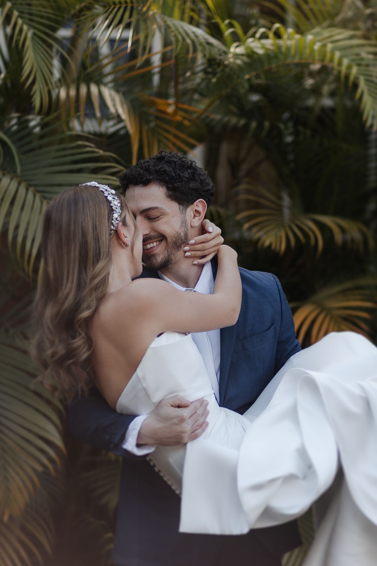 A romantic wedding moment captured outdoors with palm trees in the background as a couple shares an intimate kiss.
