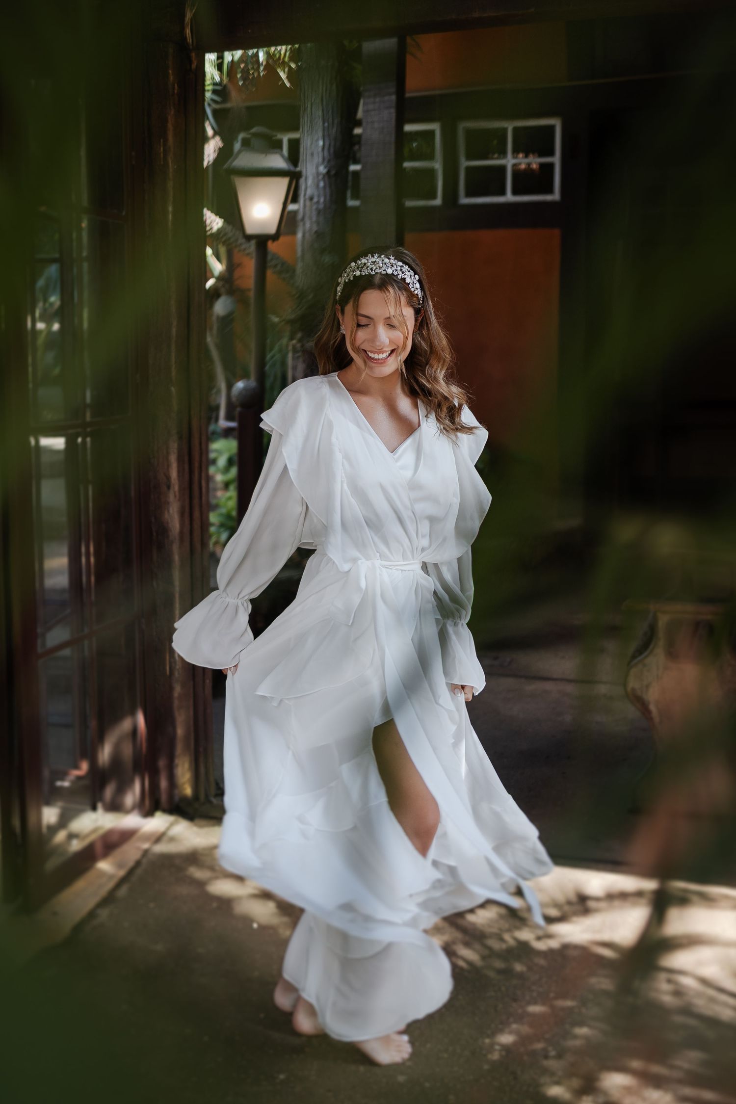 A person in a flowing white dress twirls playfully in dappled sunlight creating an ethereal outdoor photoshoot moment.