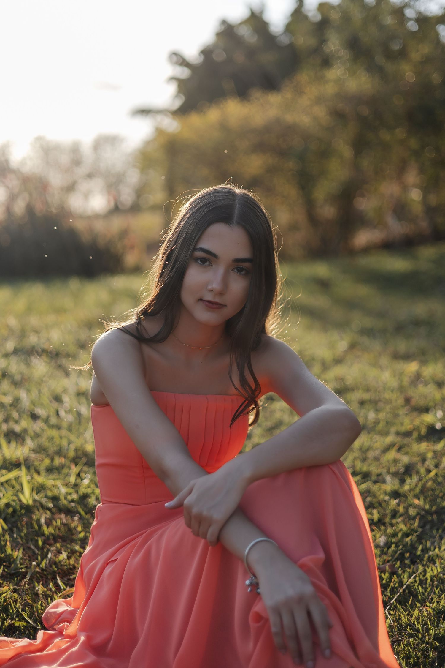 A person in a coral dress sits in a grassy field during golden hour sunlight.