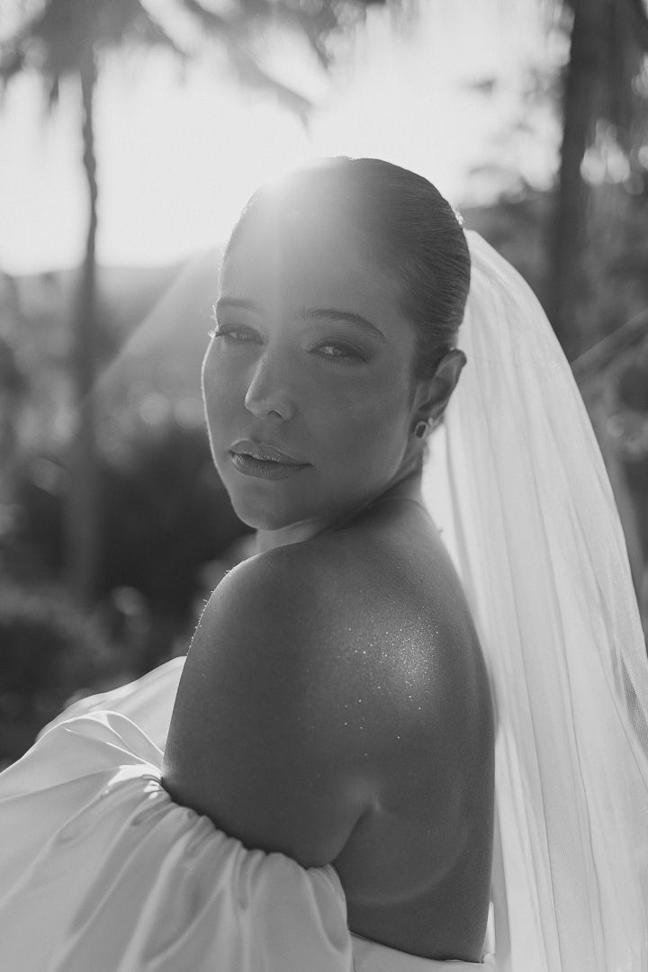 A black and white portrait of a bride in a white dress with a veil against a soft, blurred background.