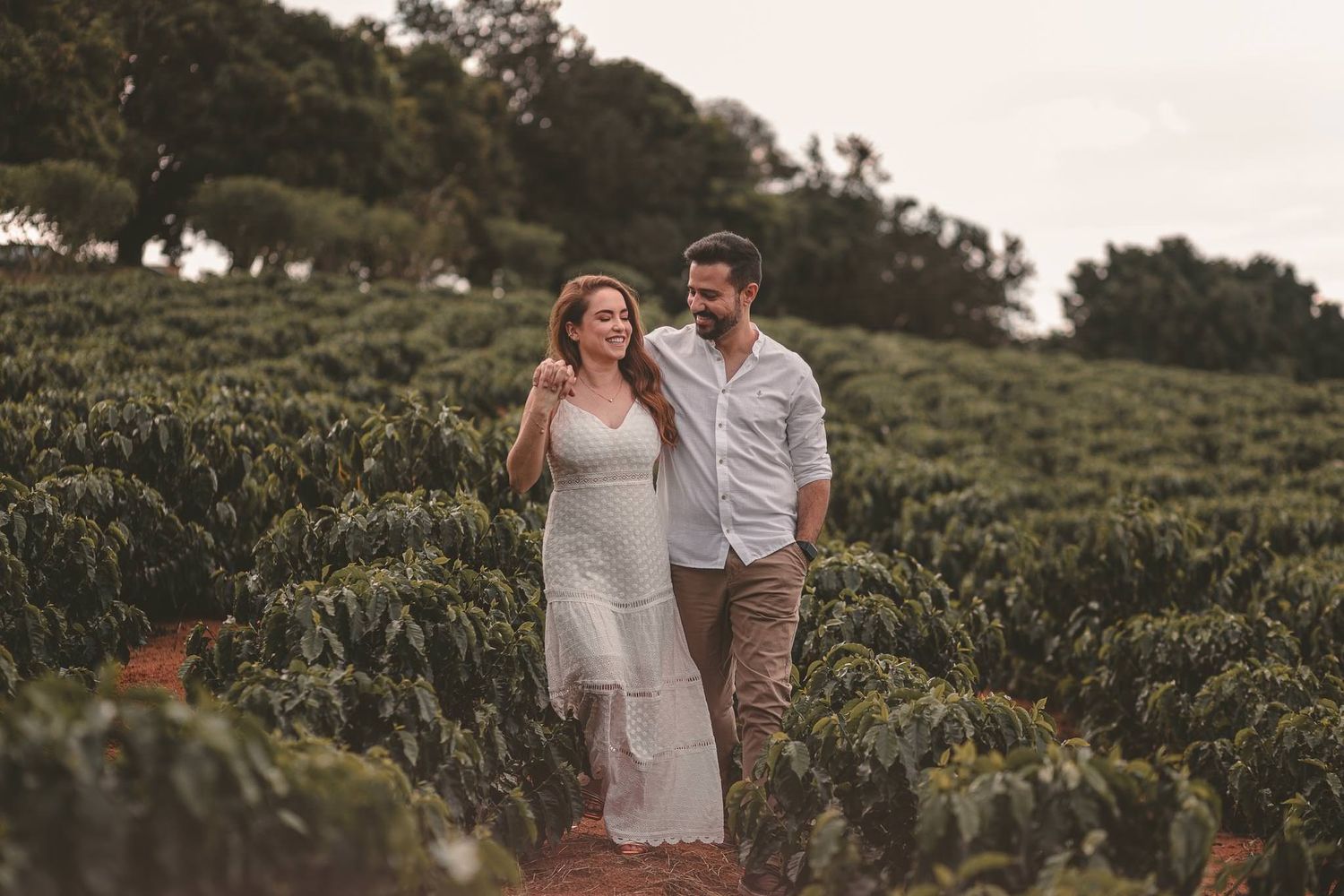A couple walking together and laughing while exploring a scenic hillside vineyard at sunset.