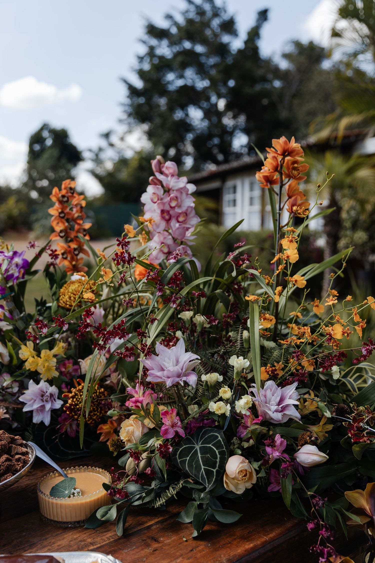 Beautiful floral arrangement with pink, orange, and yellow blooms displayed on a rustic wooden surface in an outdoor garden setting.