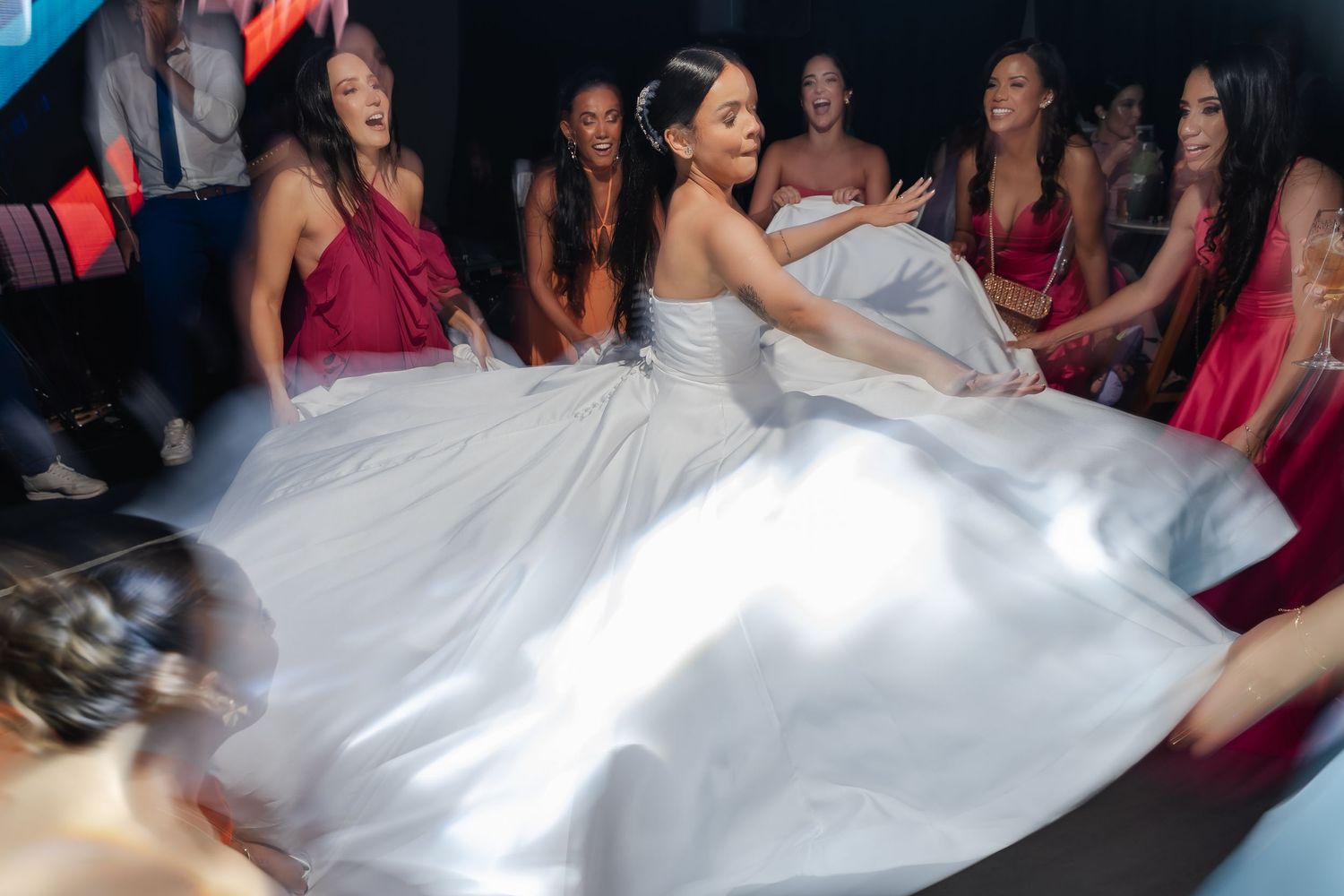 A bride in a white wedding dress spins on the dance floor surrounded by bridesmaids wearing red dresses.