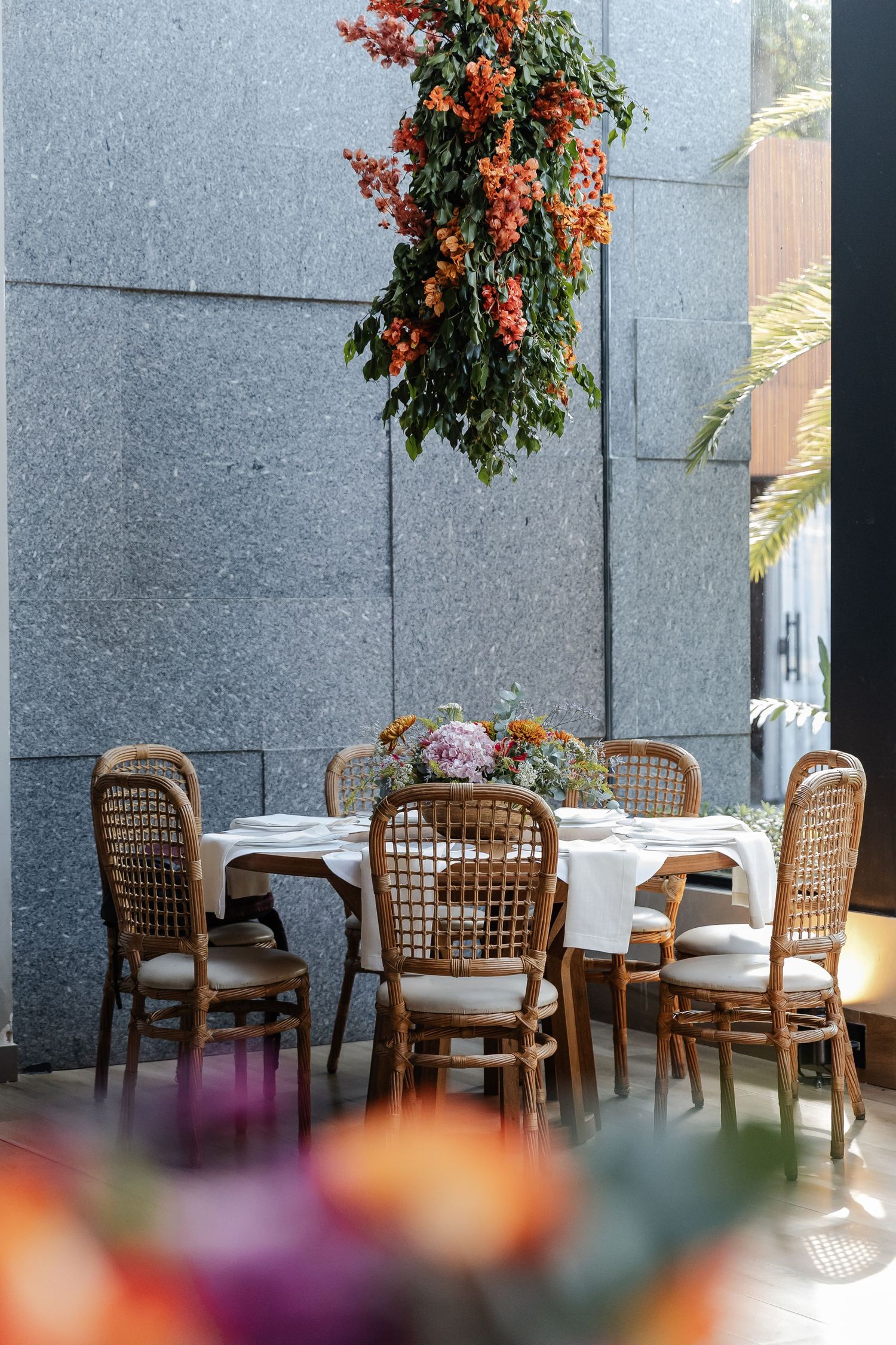 casamento em Belo Horizonte, casamento Elegant outdoor dining setup with wicker chairs and hanging orange flowers against a grey stone wall.