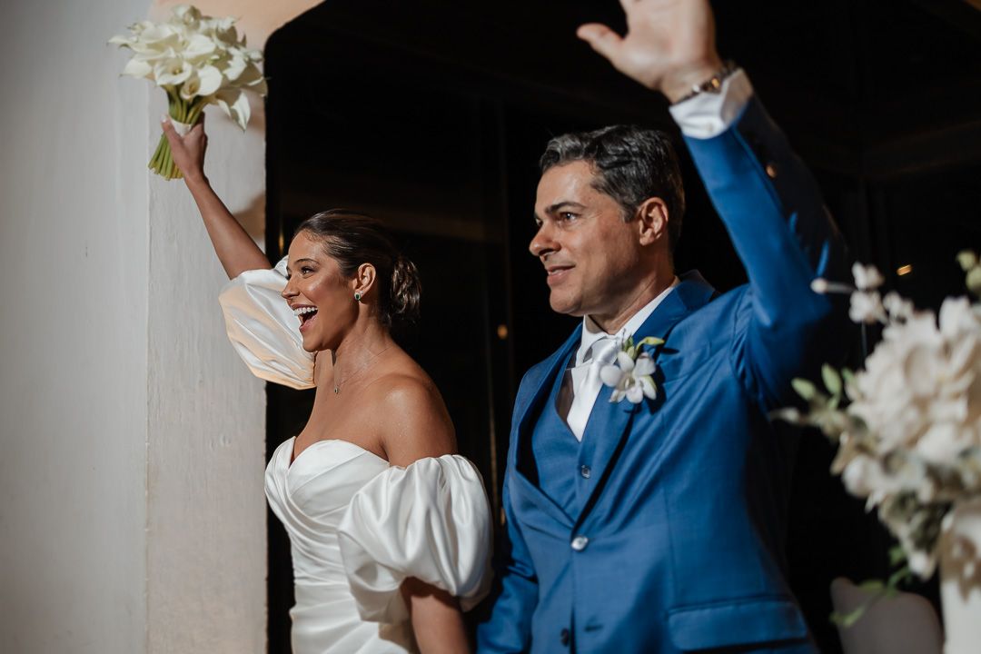 A joyful wedding celebration with white flowers as the couple raises their arms in celebration while exiting the ceremony.