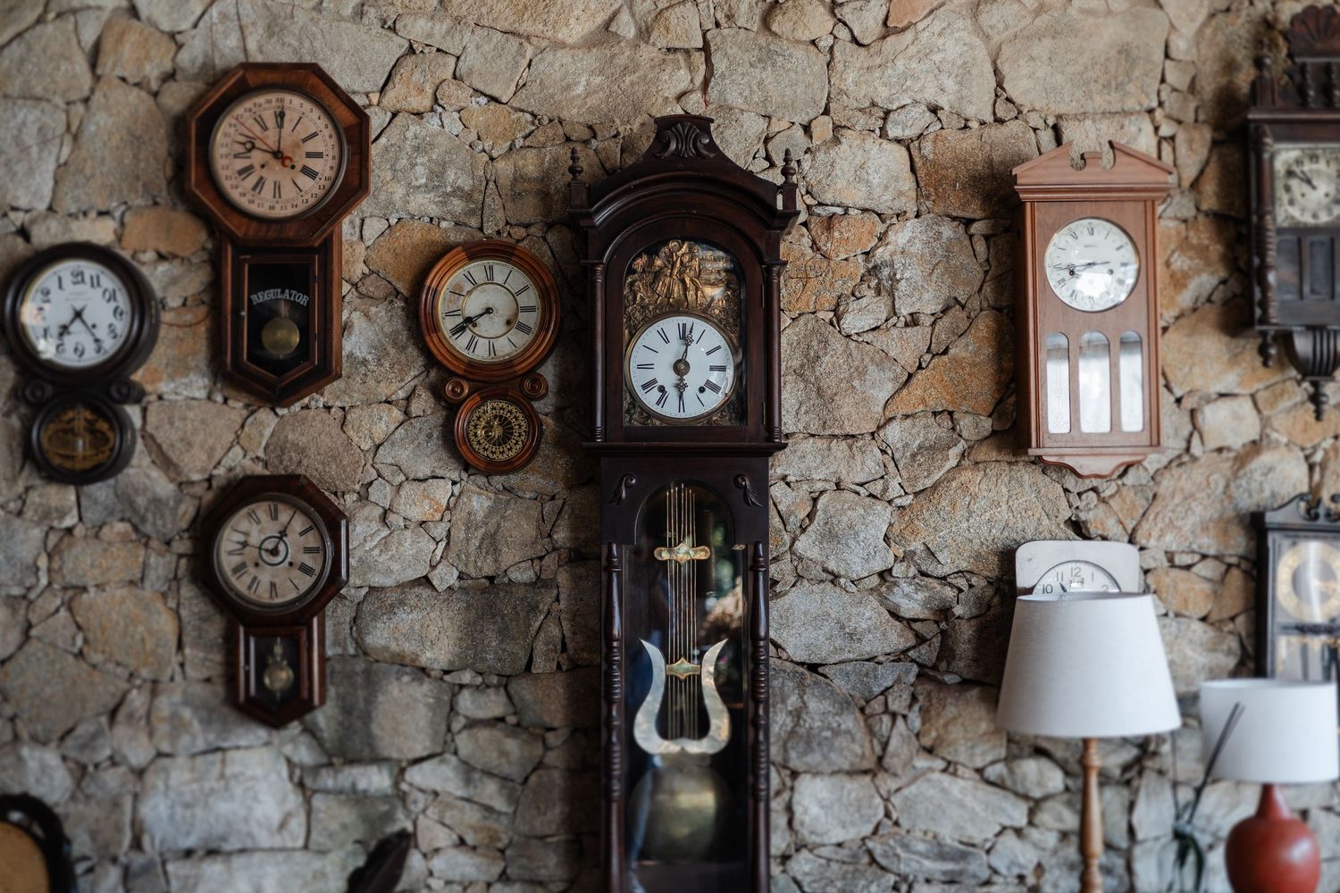 Collection of vintage wall clocks displayed against a rustic stone wall, creating an antique timekeeper gallery.