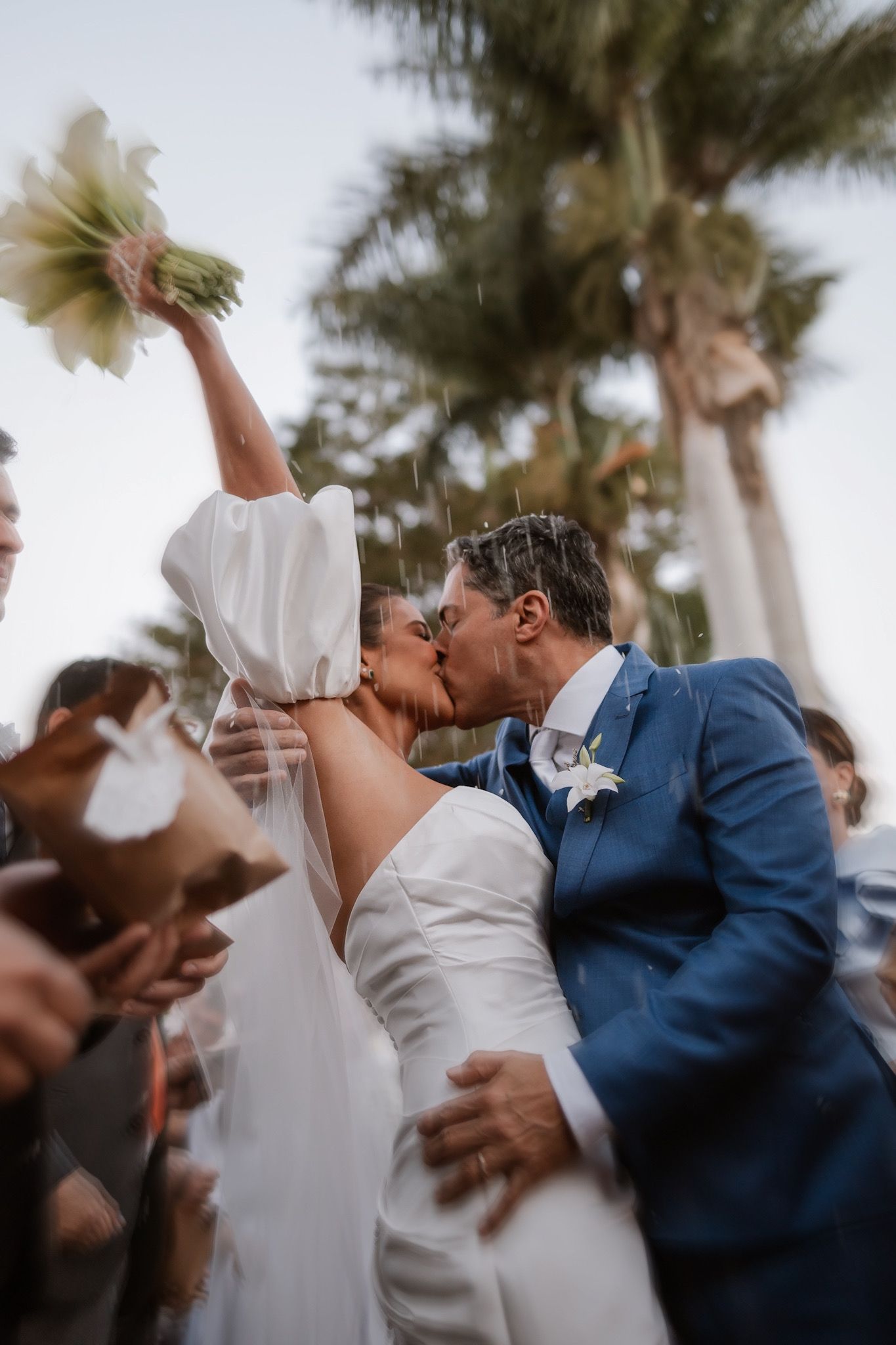 A joyful wedding ceremony kiss captured outdoors with palm trees in the background.