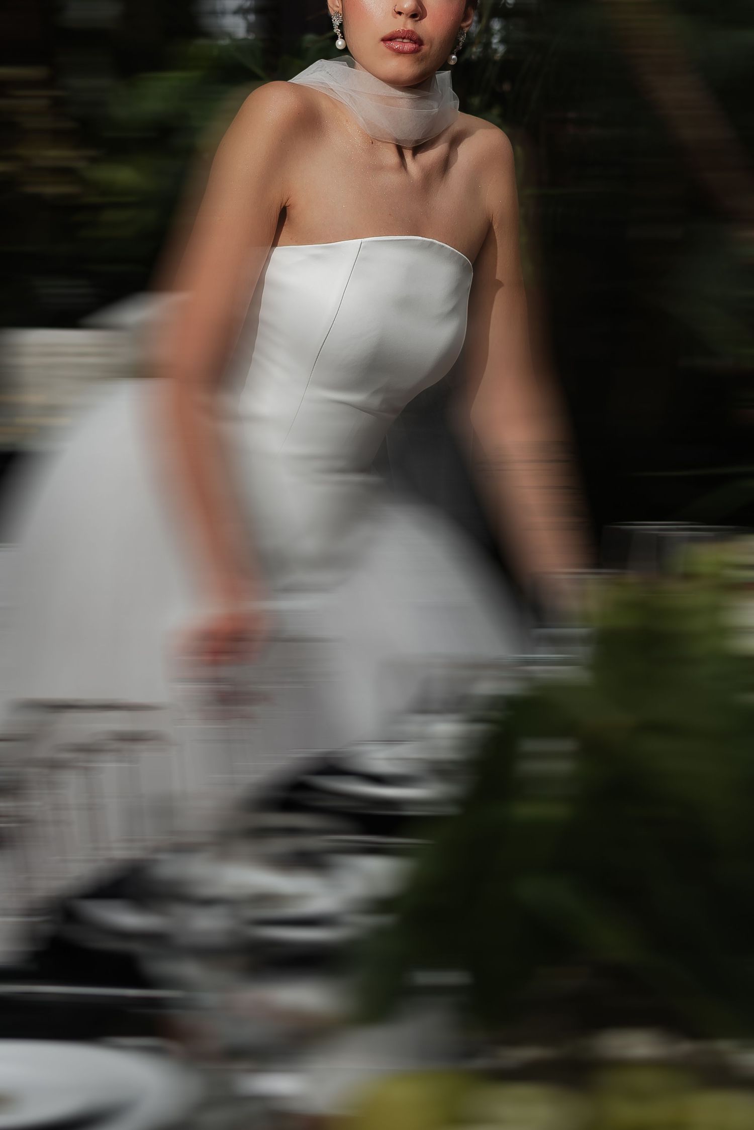 A person in a white strapless wedding dress poses outdoors with motion blur effects in a garden setting.