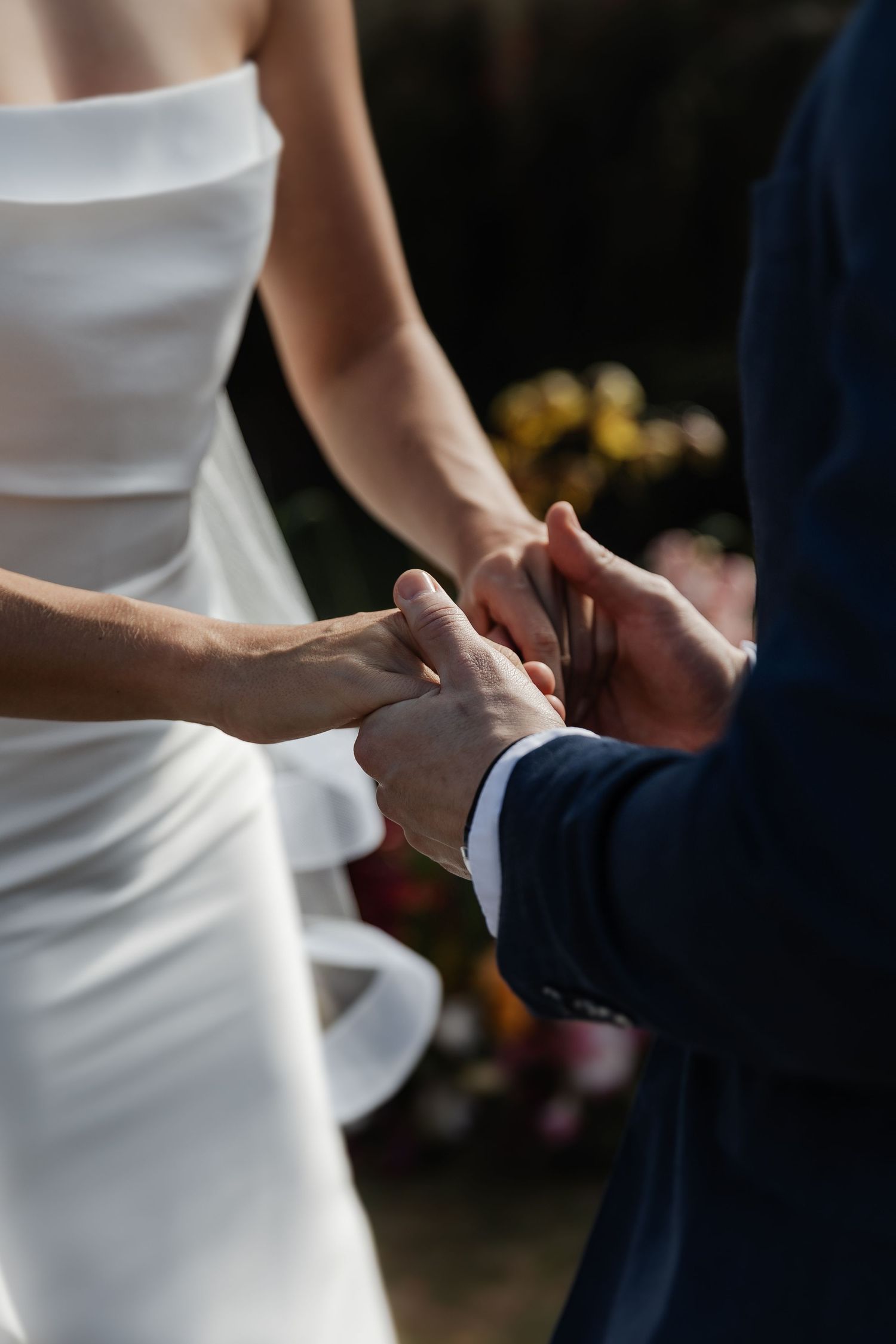 Close-up shot of bride and groom holding hands during wedding ceremony, bride wearing elegant white dress.