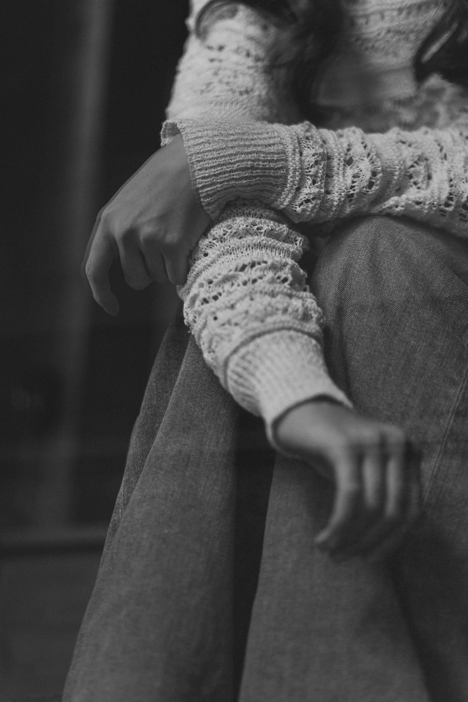 Black and white photo of arms crossed over knees wearing cozy knit sweater sleeves and jeans.
