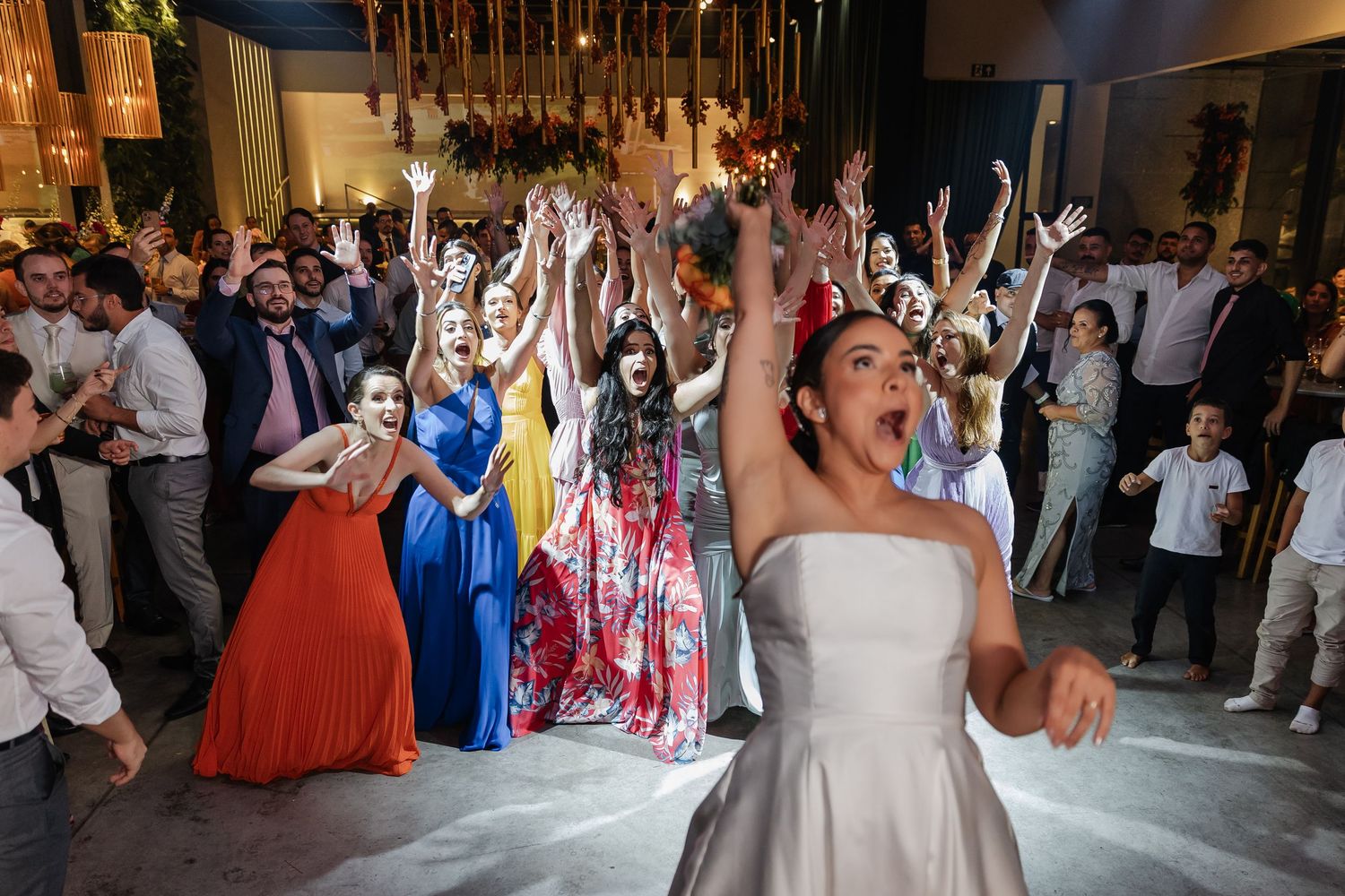 Energetic wedding celebration with guests dancing and cheering on a dance floor at an indoor reception venue.
