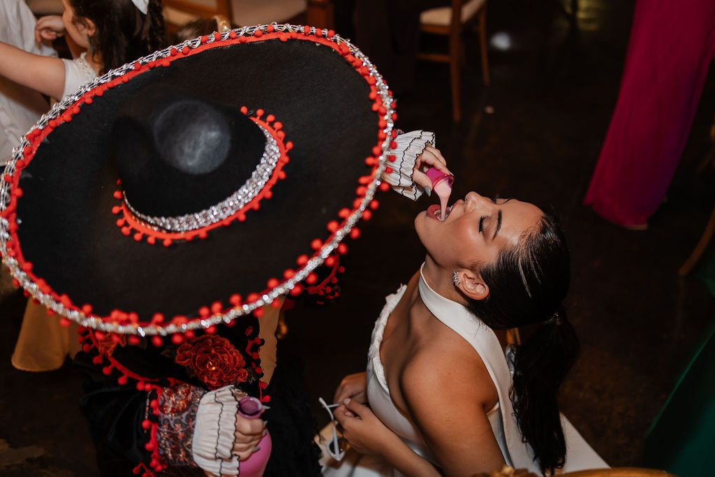 A joyful celebratory moment as a black sombrero with red pom poms is held above someone dancing at a party.