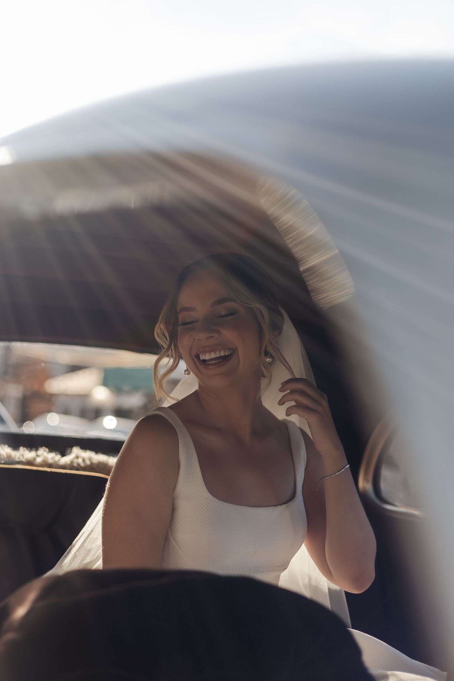 A candid portrait through a car window shows someone in a white tank top laughing joyfully in warm sunlight.