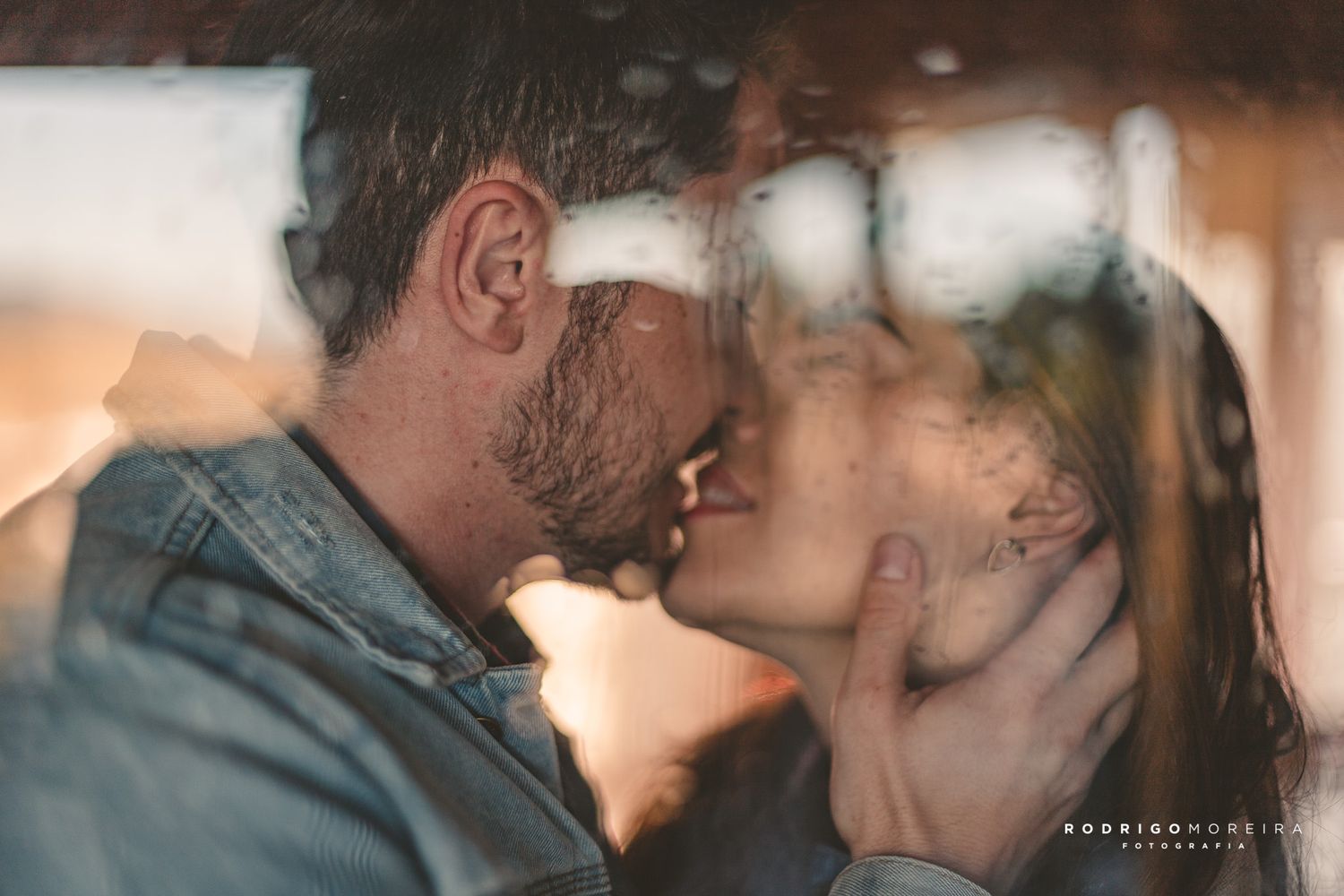 Romantic couple sharing an intimate kiss through soft window light and hazy glass.
