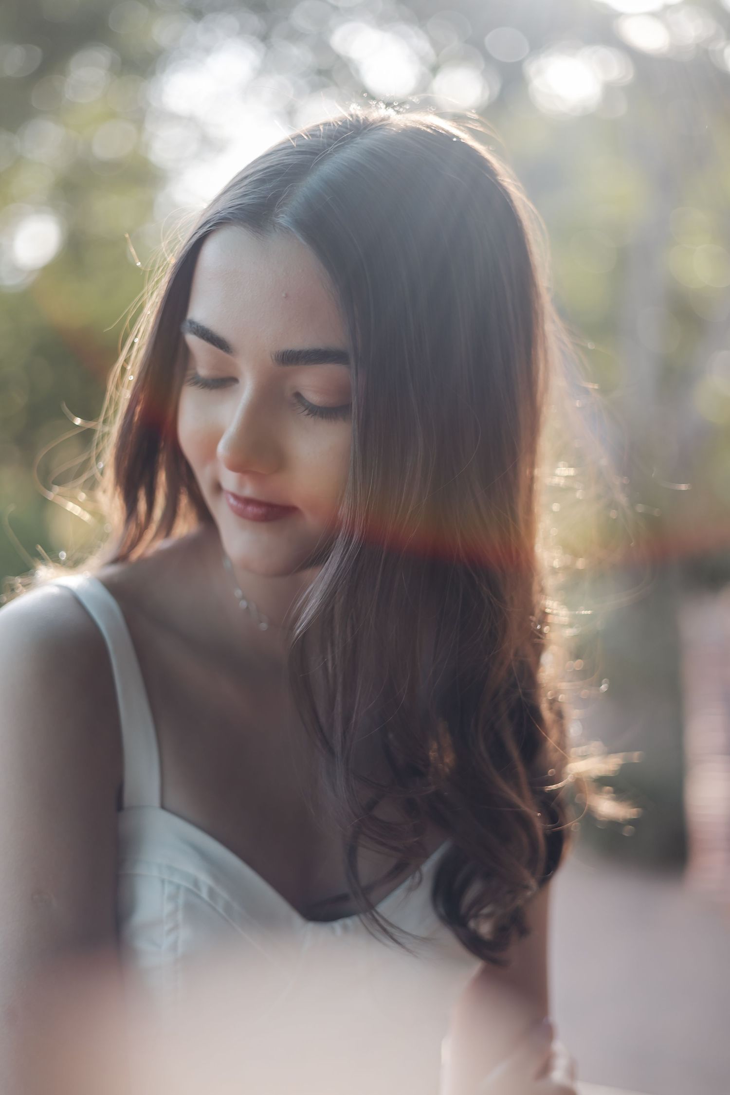 A dreamy portrait in soft sunlight shows long dark hair and a white top with ethereal backlight creating a romantic mood.