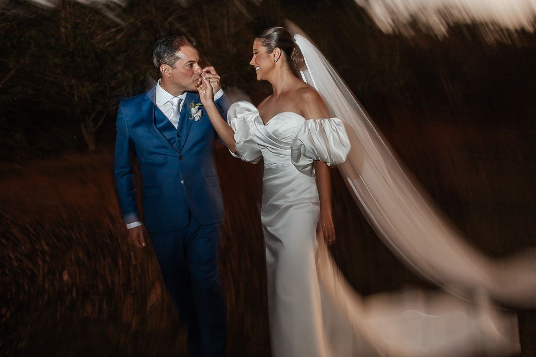 A bride and groom share an intimate moment in a field at sunset, with her flowing veil catching the light.