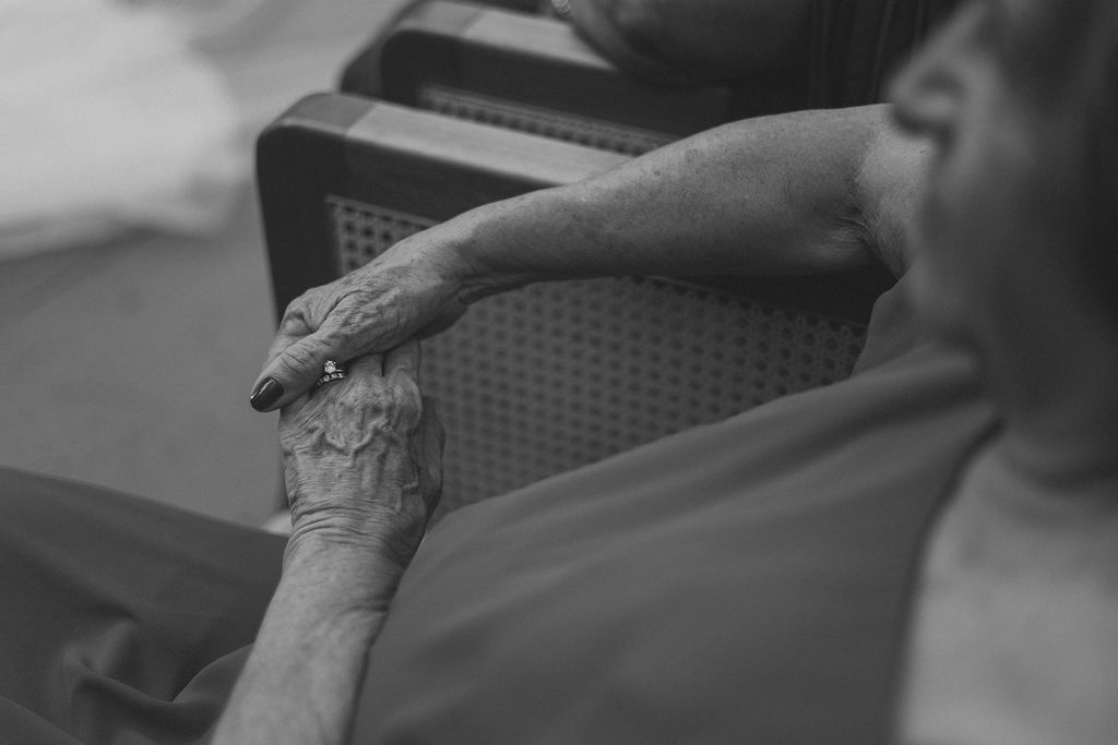 A close-up black and white shot of an elderly person's hand resting on a chair.