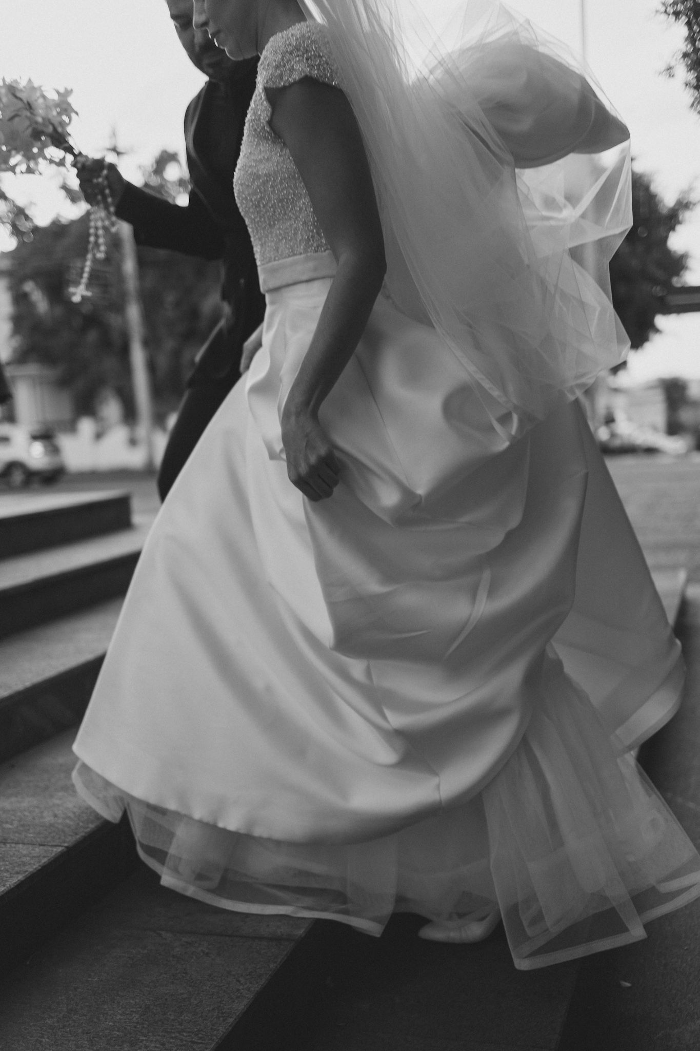A black and white close-up of a flowing wedding dress with lace cap sleeves and tulle layers in motion.