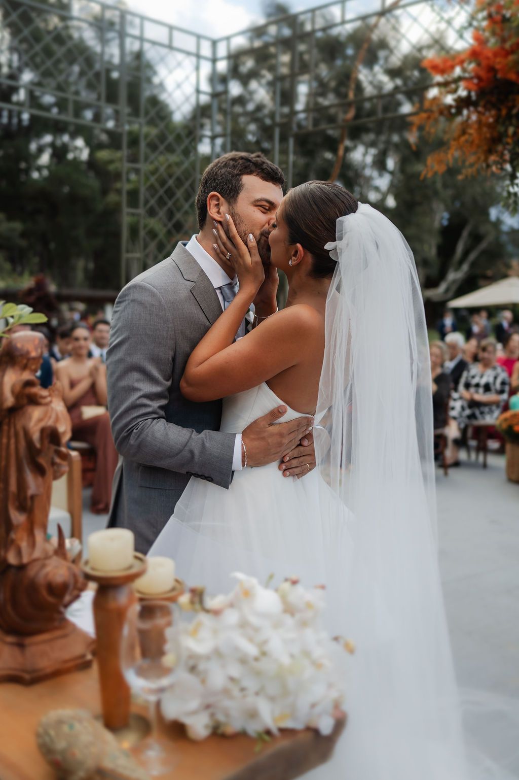 Casamento na Fazenda VintA romantic wedding ceremony kiss between newlyweds at an outdoor venue with autumn foliage and decorative elements.