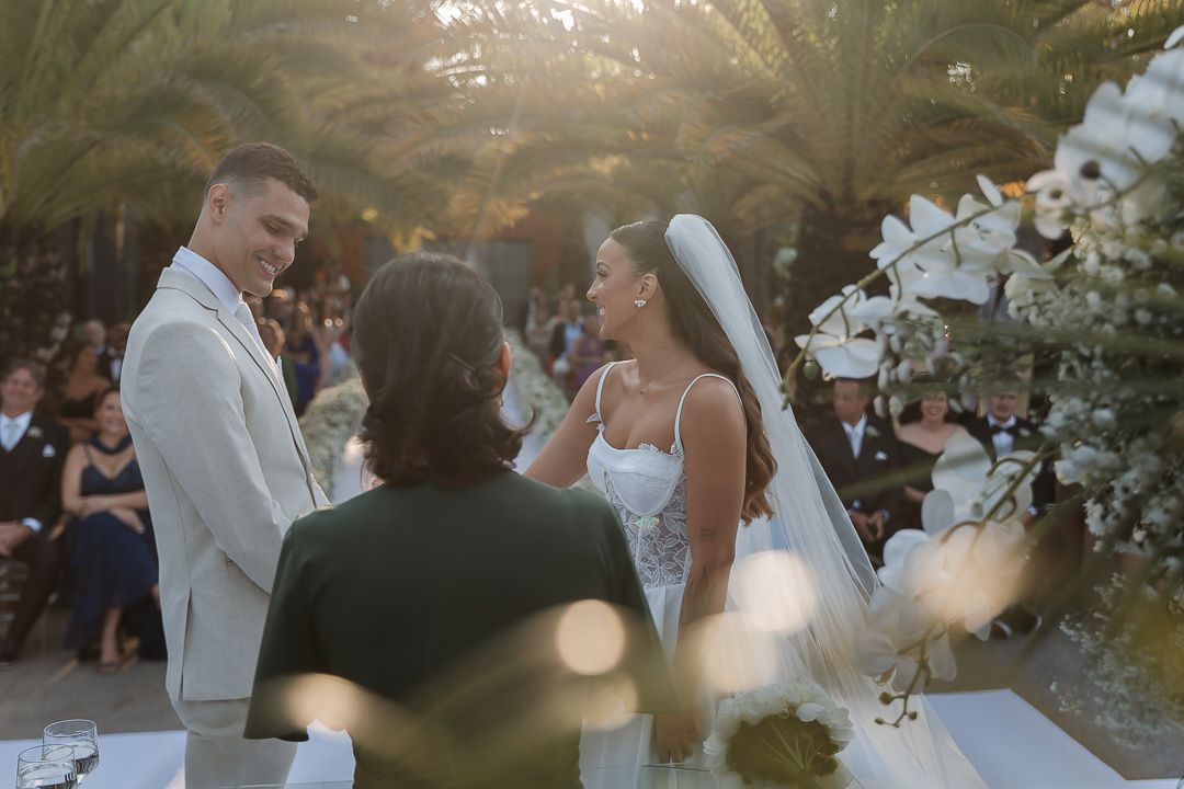 Outdoor wedding ceremony under palm trees with couple and officiant at altar.