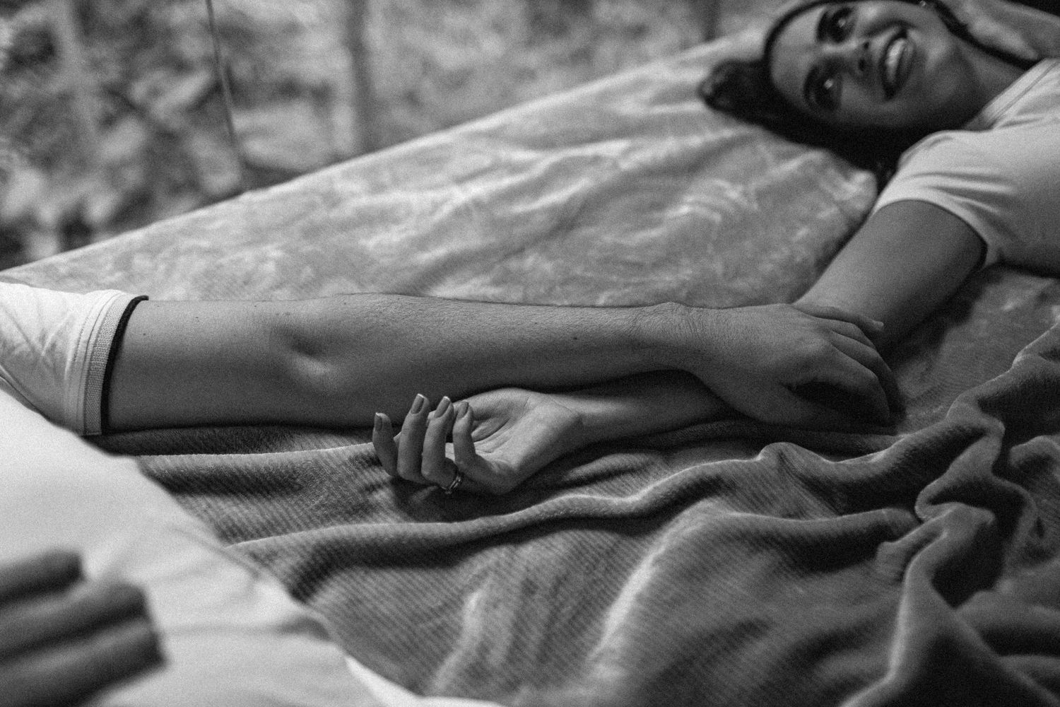 A black and white image shows hands clasped together while resting on a blanket.