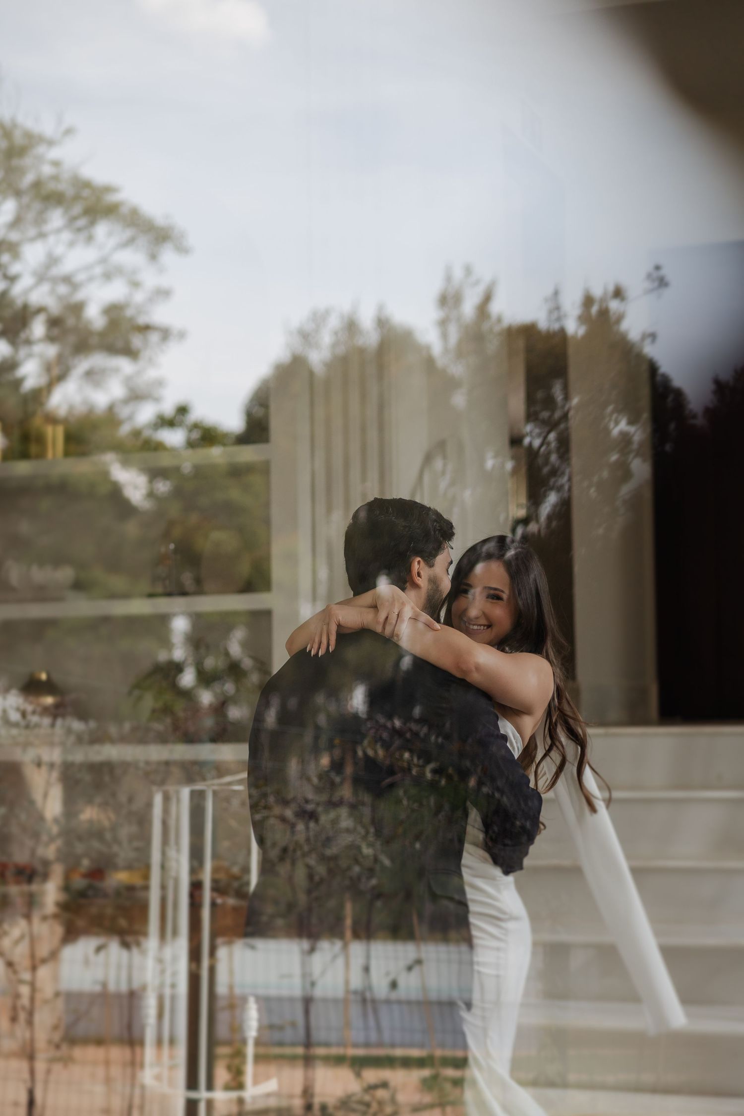 A romantic couple embraces on a staircase with soft lighting and reflective glass creating a dreamy atmosphere.