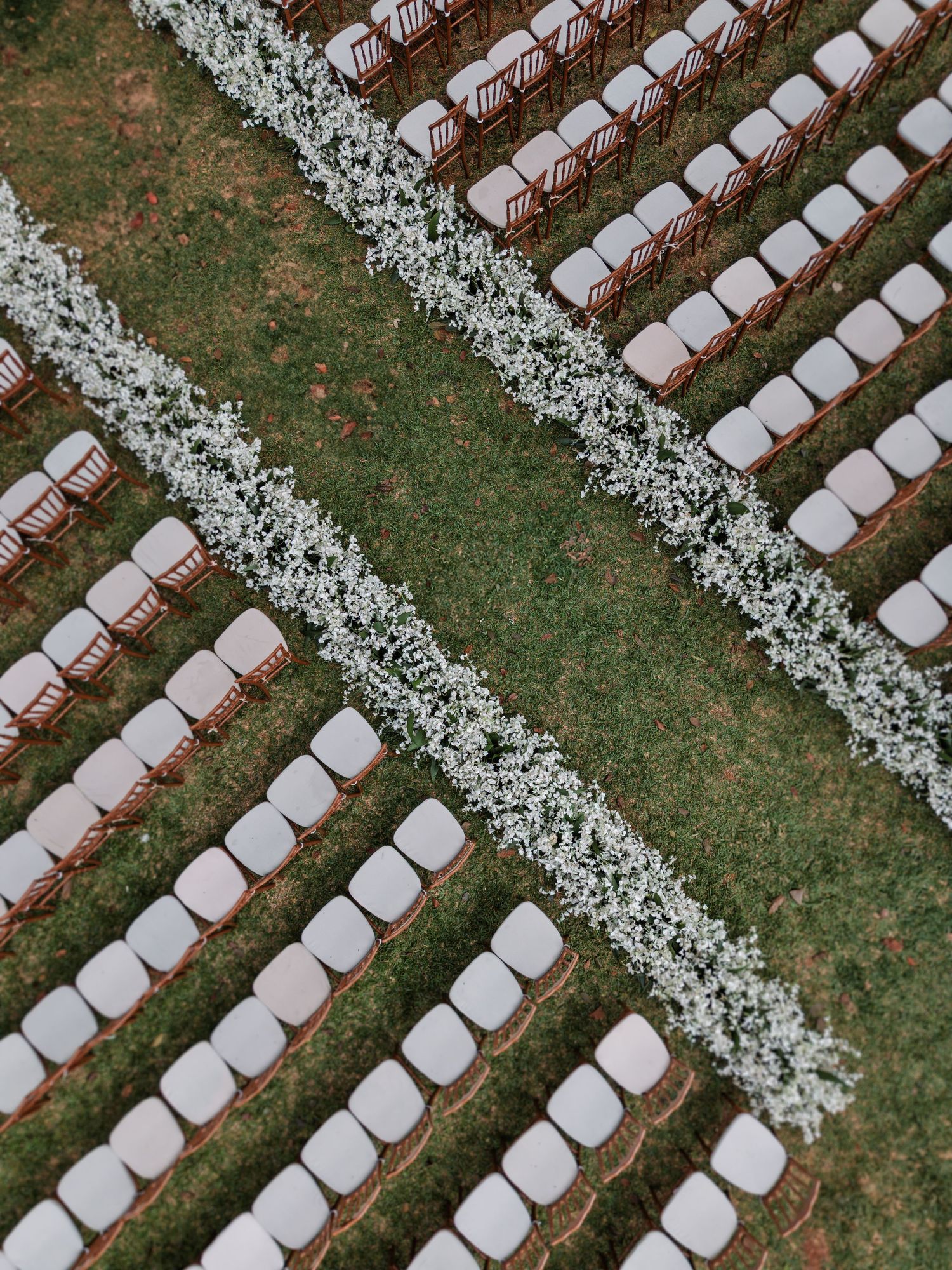 Aerial view of outdoor wedding ceremony seating arranged in diagonal rows with delicate white floral aisle runners.