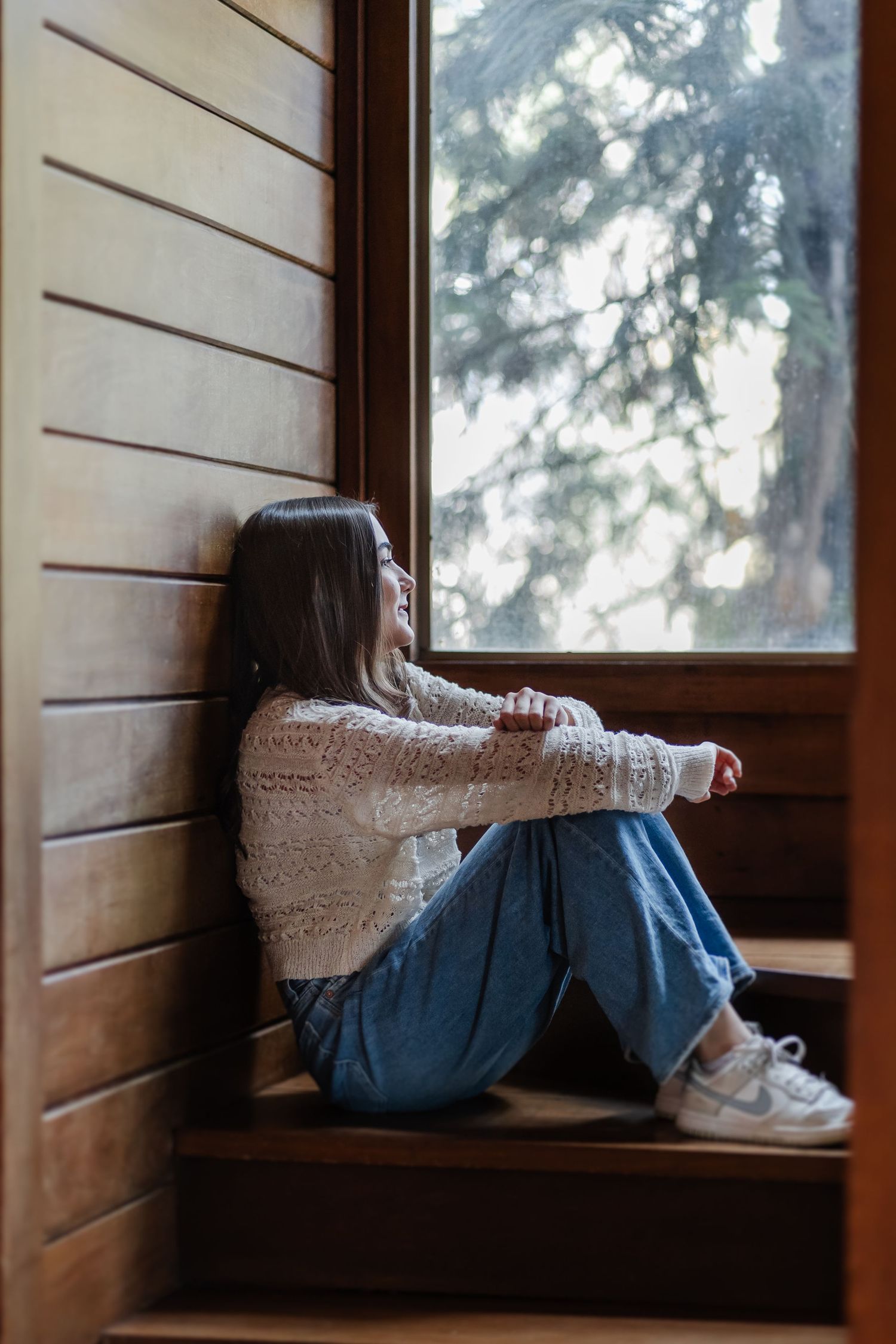 Window seat in wooden cabin with white lace dress and denim jeans draped over edge against misty forest backdrop.