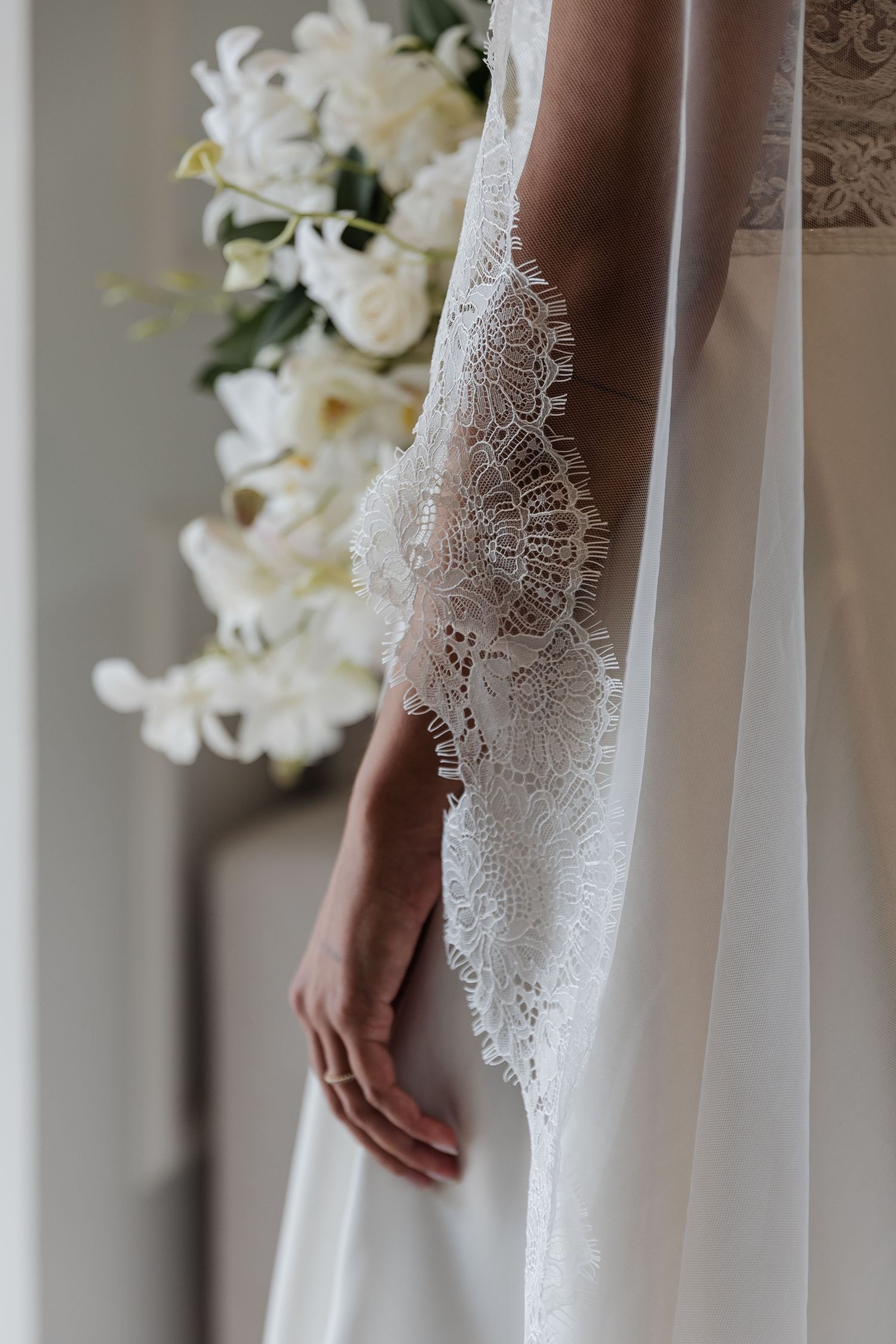 Close-up detail of delicate white lace applique on an elegant wedding dress with flowing fabric.