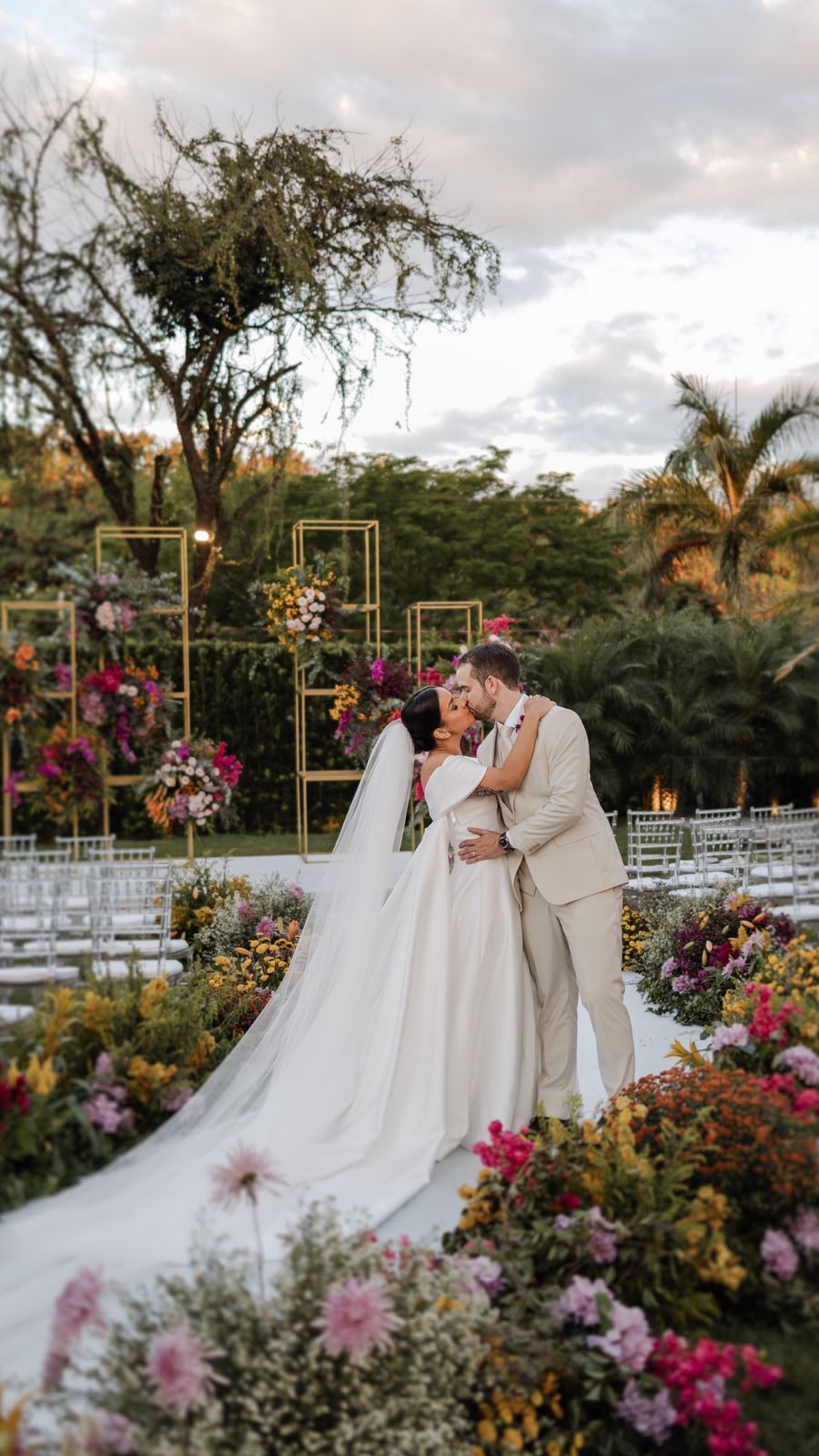 A couple shares an intimate moment in a beautiful garden wedding ceremony setup with colorful flowers and geometric decor.