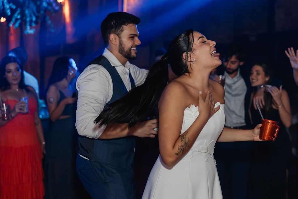 A wedding couple dances enthusiastically on the dance floor at their reception celebration with blue lighting in the background.