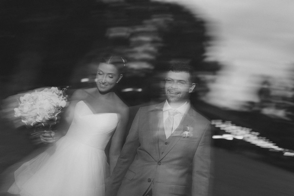 A black and white romantic wedding photo showing a couple walking together with motion blur effects.