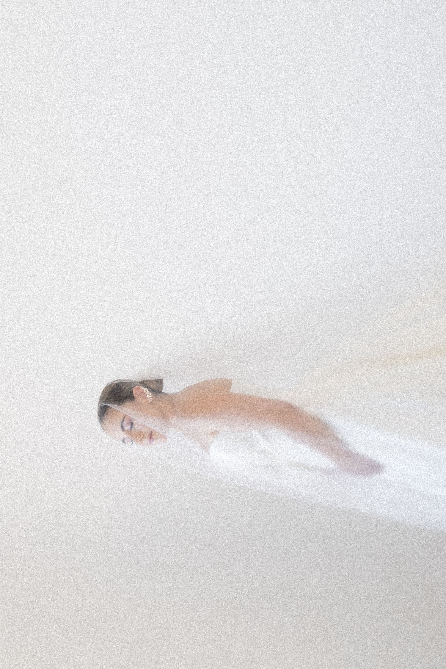 A figure draped in soft white fabric lies peacefully against a minimalist white background creating an ethereal mood.