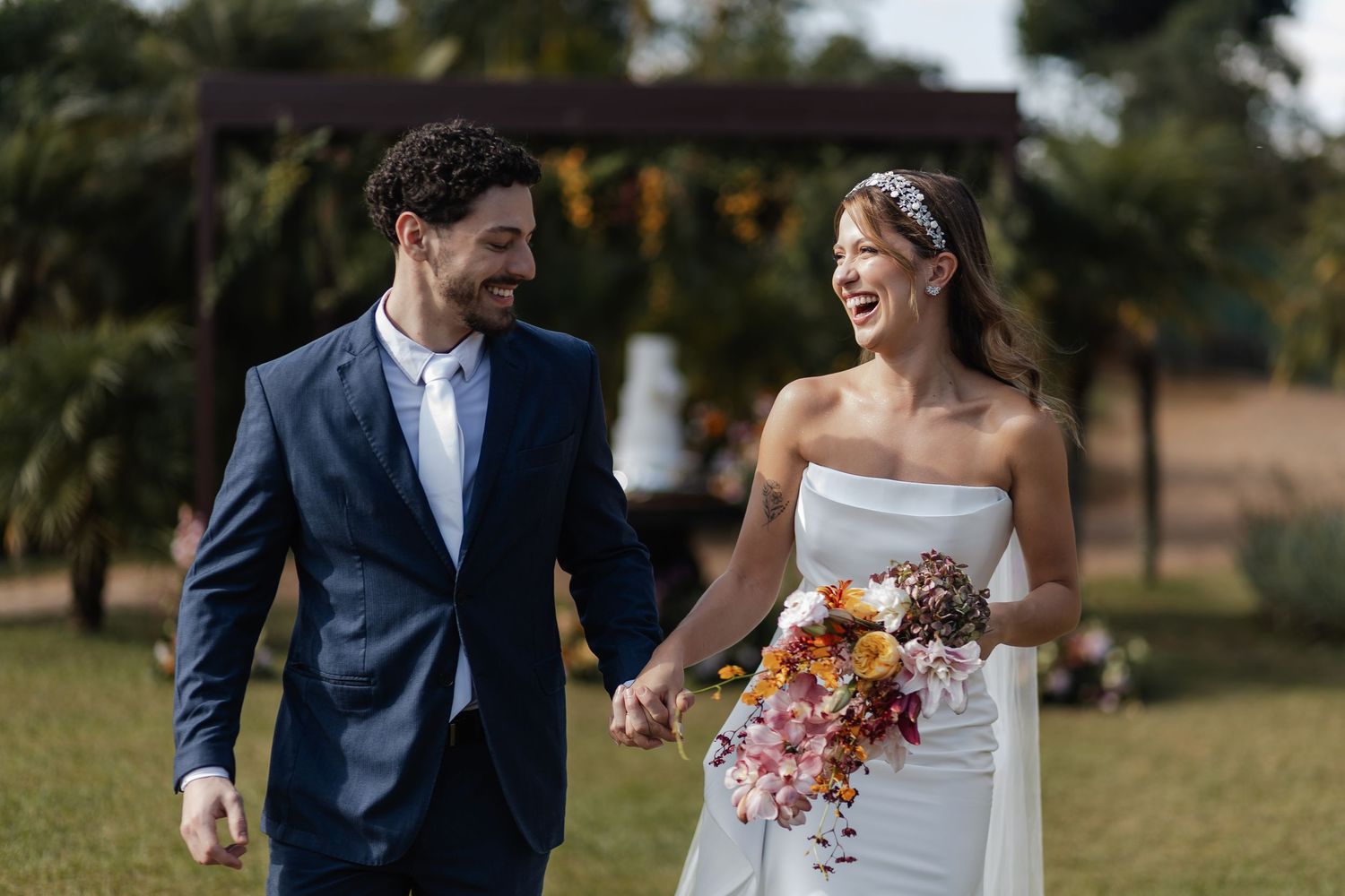 A happy couple walking and laughing together in an outdoor setting while dressed in formal wedding attire.