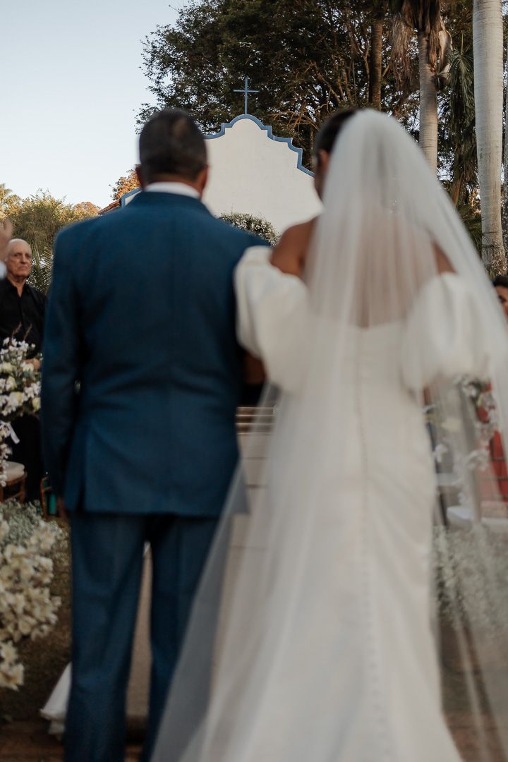 Couple stands at altar during outdoor wedding ceremony with white church and palm trees in background.