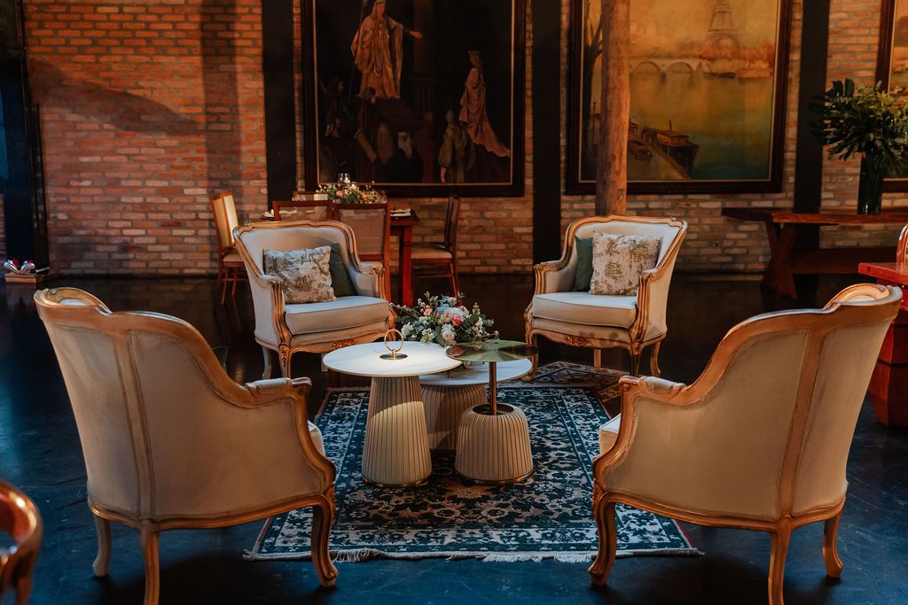 Cozy seating area with plush cream armchairs arranged around white side tables on a blue patterned rug in dim lighting.