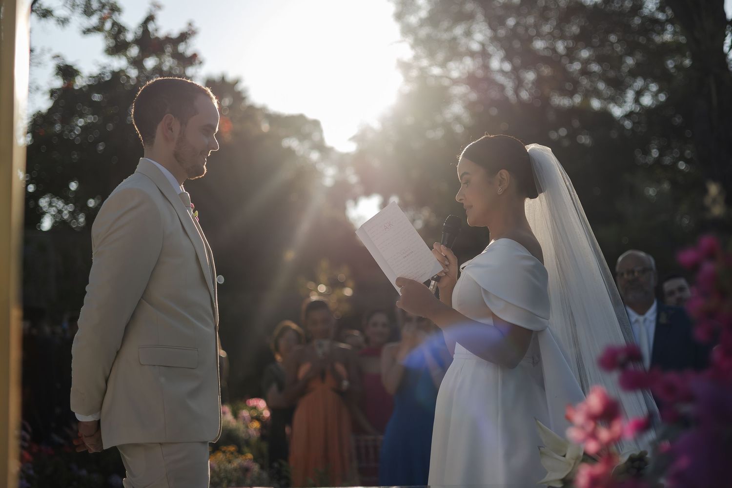 Beautiful outdoor wedding ceremony during sunset with silhouetted newlyweds and guests against glowing sky.