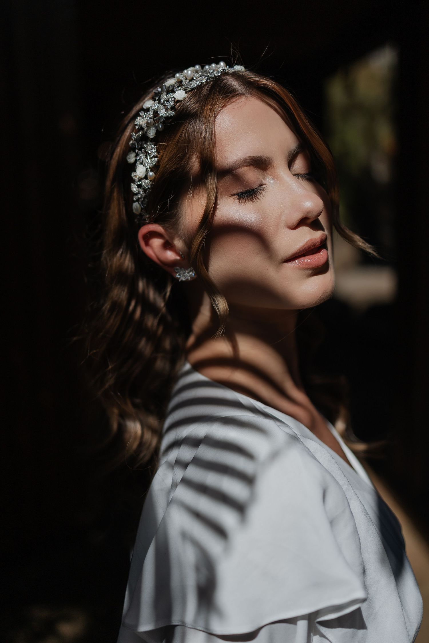 Artistic portrait showing serene expression in dramatic lighting with floral headpiece and white silk robe.