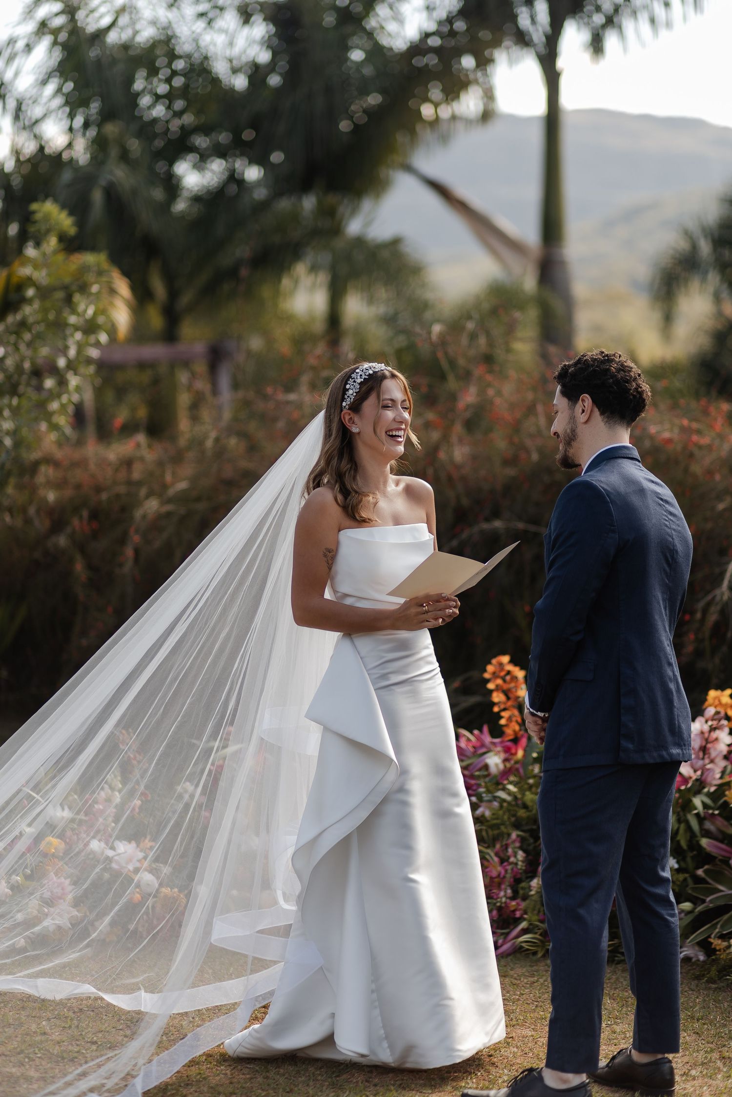 A couple celebrates their outdoor wedding with joyful interactions against a scenic natural backdrop with palm trees and flowers.
