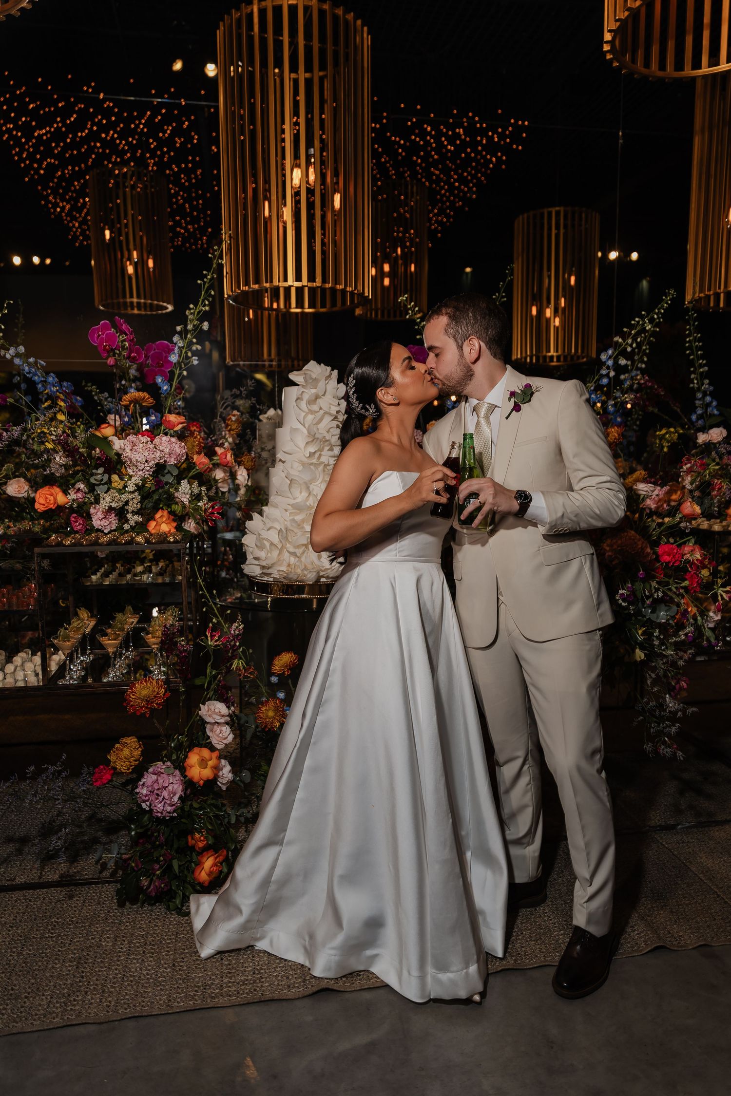 Elegant wedding reception decor with string lights, bamboo chandeliers and colorful floral arrangements at night.